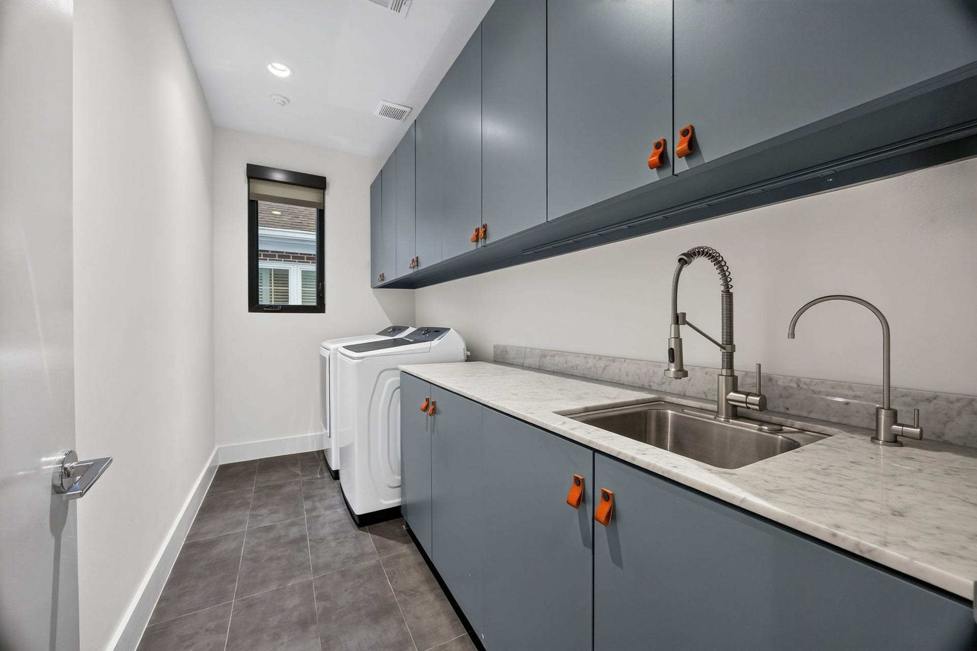 6002 Valley Forge Drive, Houston, TX 77057 Modern laundry room with sleek blue cabinetry, marble countertop, dual sinks, and high-efficiency washer and dryer.