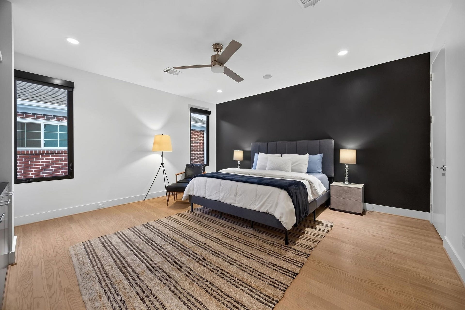 6002 Valley Forge Drive, Houston, TX 77057 Spacious bedroom featuring a modern black accent wall, cozy lighting, and elegant hardwood floors, offering a serene retreat.