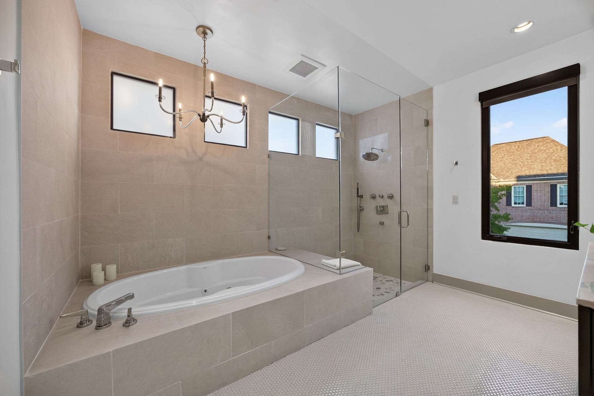 6002 Valley Forge Drive, Houston, TX 77057 Luxurious bathroom featuring a spacious soaking tub, elegant chandelier, and a sleek glass-enclosed shower, all set against stylish tile work.
