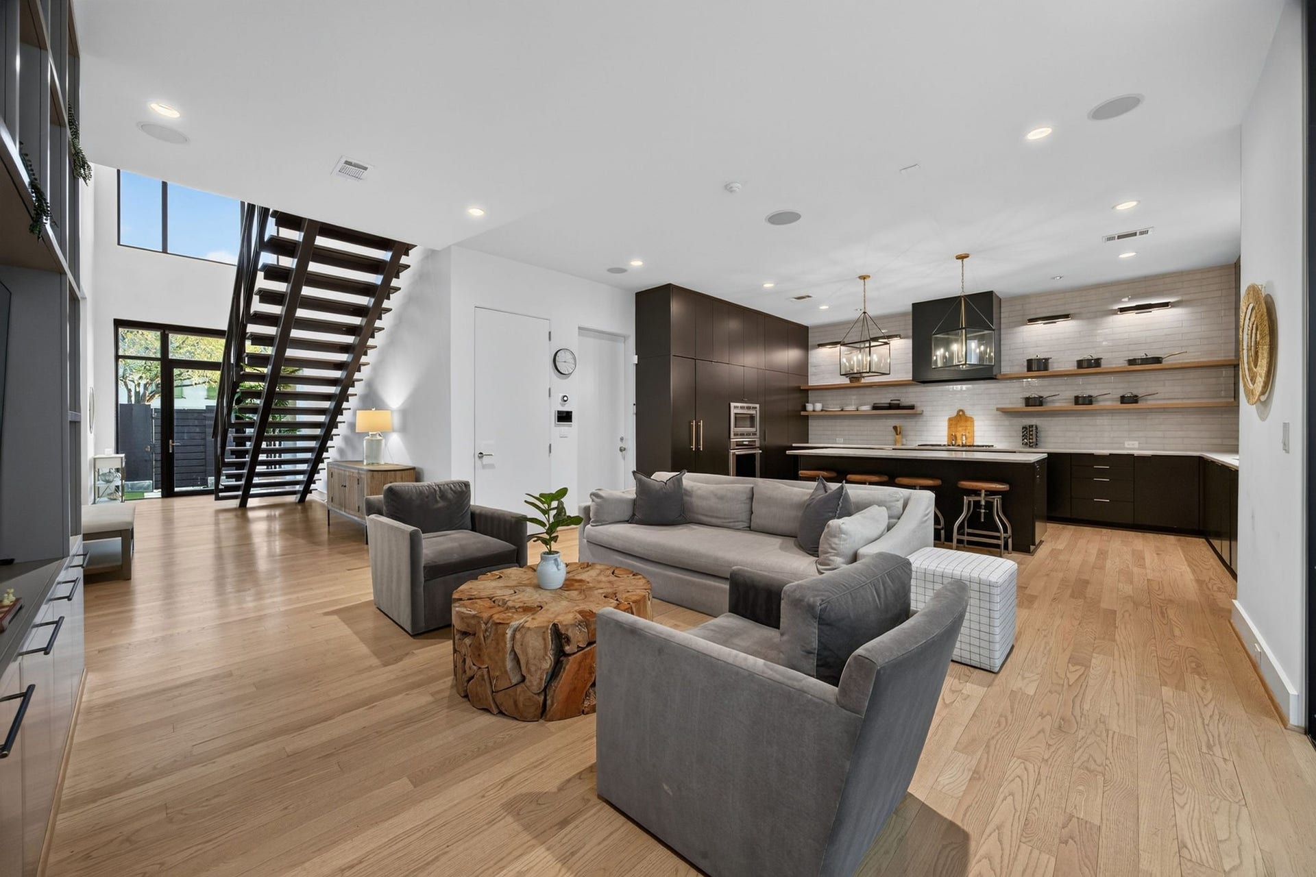 6002 Valley Forge Drive, Houston, TX 77057 Spacious open-concept living area featuring a sleek modern kitchen with dark cabinetry, an inviting lounge space with ample seating, and a striking staircase leading to the upper level.