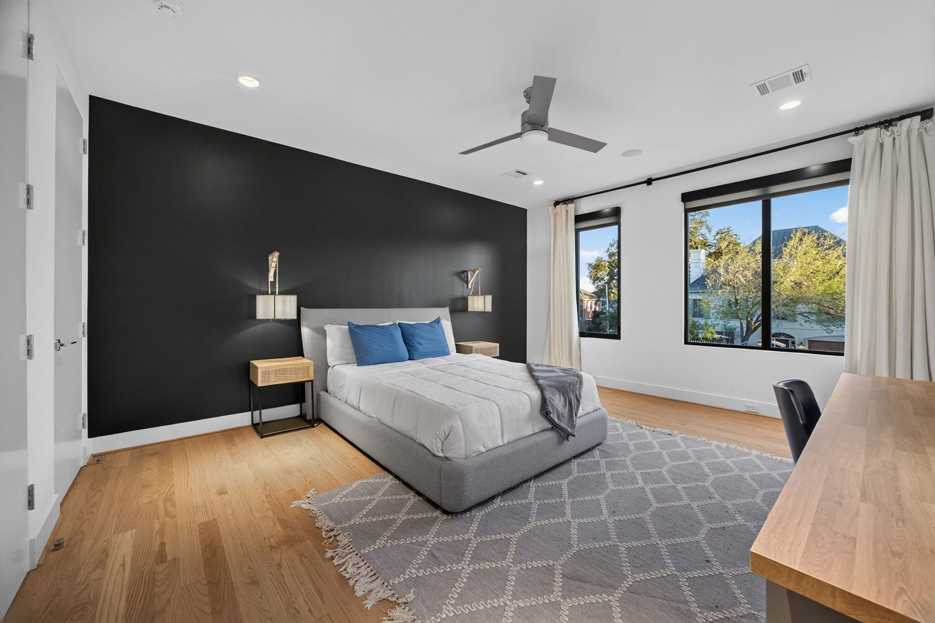 6002 Valley Forge Drive, Houston, TX 77057 Spacious bedroom with a sleek black accent wall, large windows for natural light, and modern furnishings including a cozy bed and stylish desk.