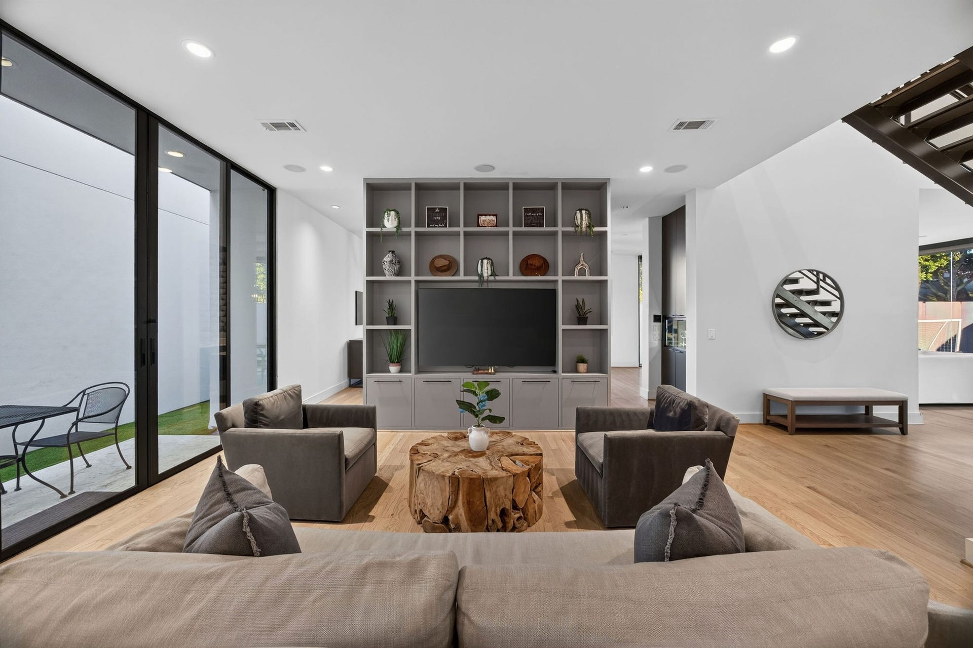 6002 Valley Forge Drive, Houston, TX 77057 Modern living room with sleek built-in shelving, cozy seating, and large glass doors offering abundant natural light and outdoor views.