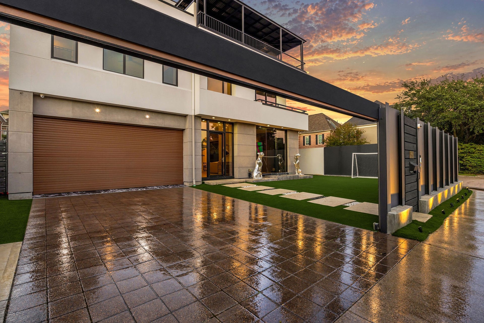 6002 Valley Forge Drive, Houston, TX 77057 Modern home featuring a sleek facade with expansive windows, a spacious garage, and a well-manicured lawn, set against a stunning sunset backdrop.