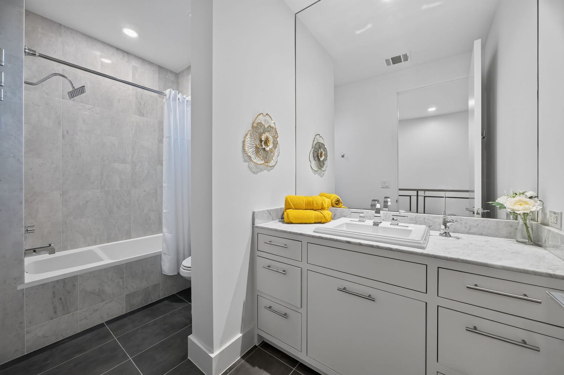 6002 Valley Forge Drive, Houston, TX 77057 Elegant bathroom featuring a sleek vanity with marble countertop, modern fixtures, and a spacious tub with a tiled surround.