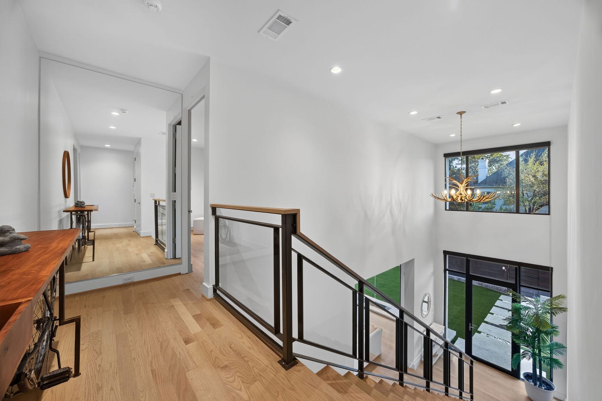 6002 Valley Forge Drive, Houston, TX 77057 Bright and modern hallway featuring sleek hardwood floors, elegant railing, and large windows that offer a view of the lush outdoors, enhancing the open, airy ambiance.