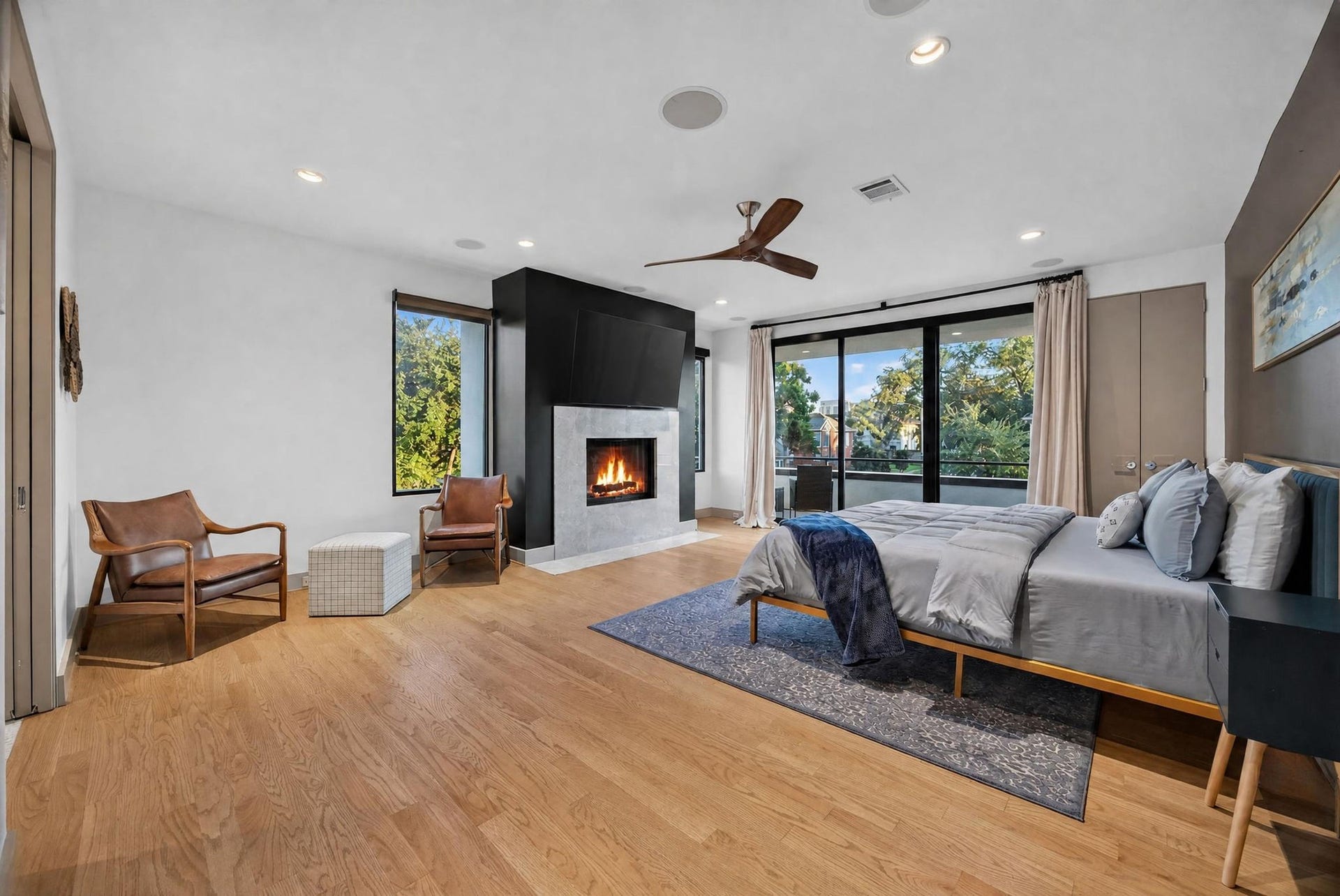 6002 Valley Forge Drive, Houston, TX 77057 Spacious bedroom featuring a sleek modern fireplace, large windows for natural light, and elegant wood flooring, creating a warm and inviting atmosphere.