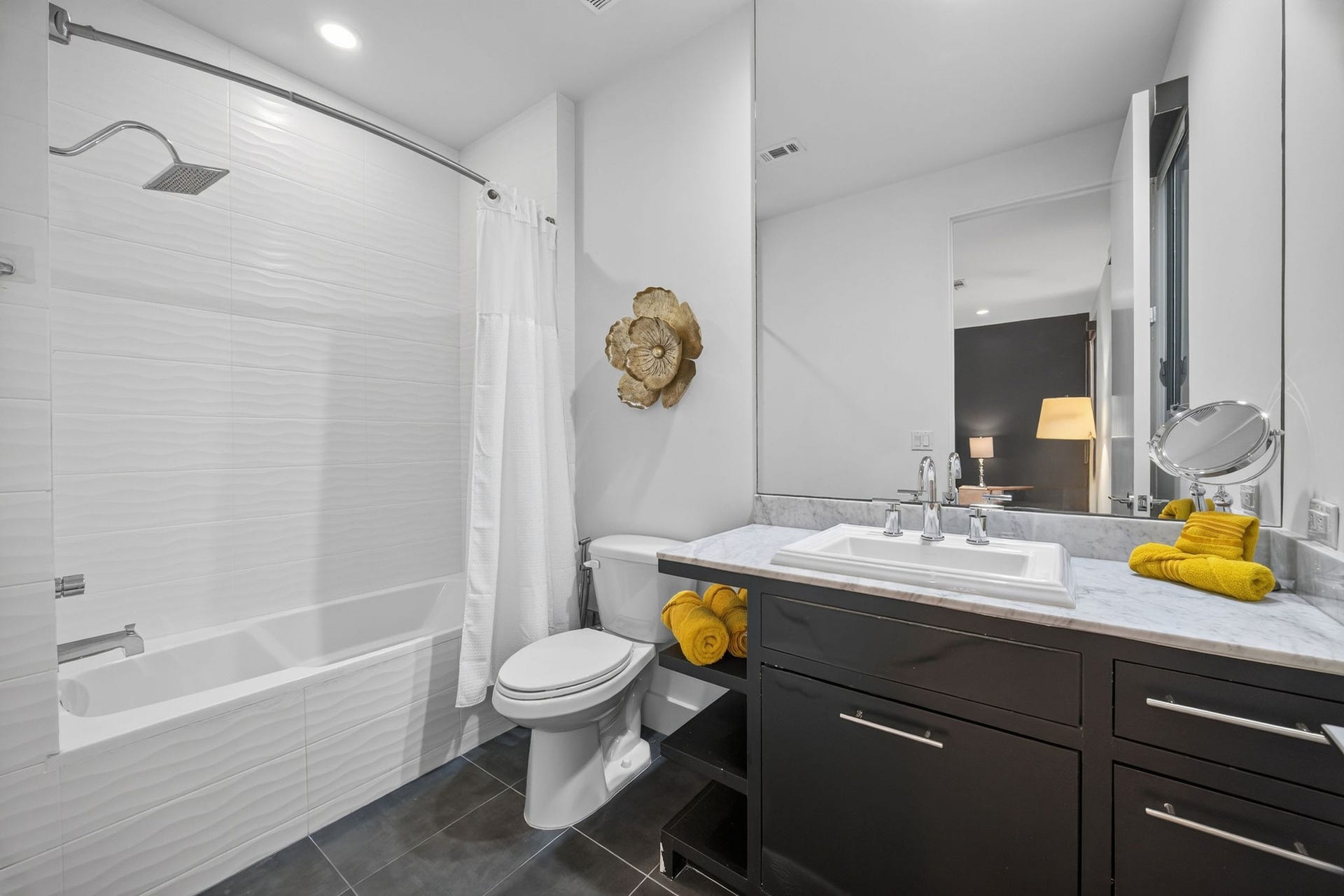 6002 Valley Forge Drive, Houston, TX 77057 Elegant bathroom featuring a modern vanity with a marble countertop, a sleek bathtub with a white tile surround, and stylish decor accents.