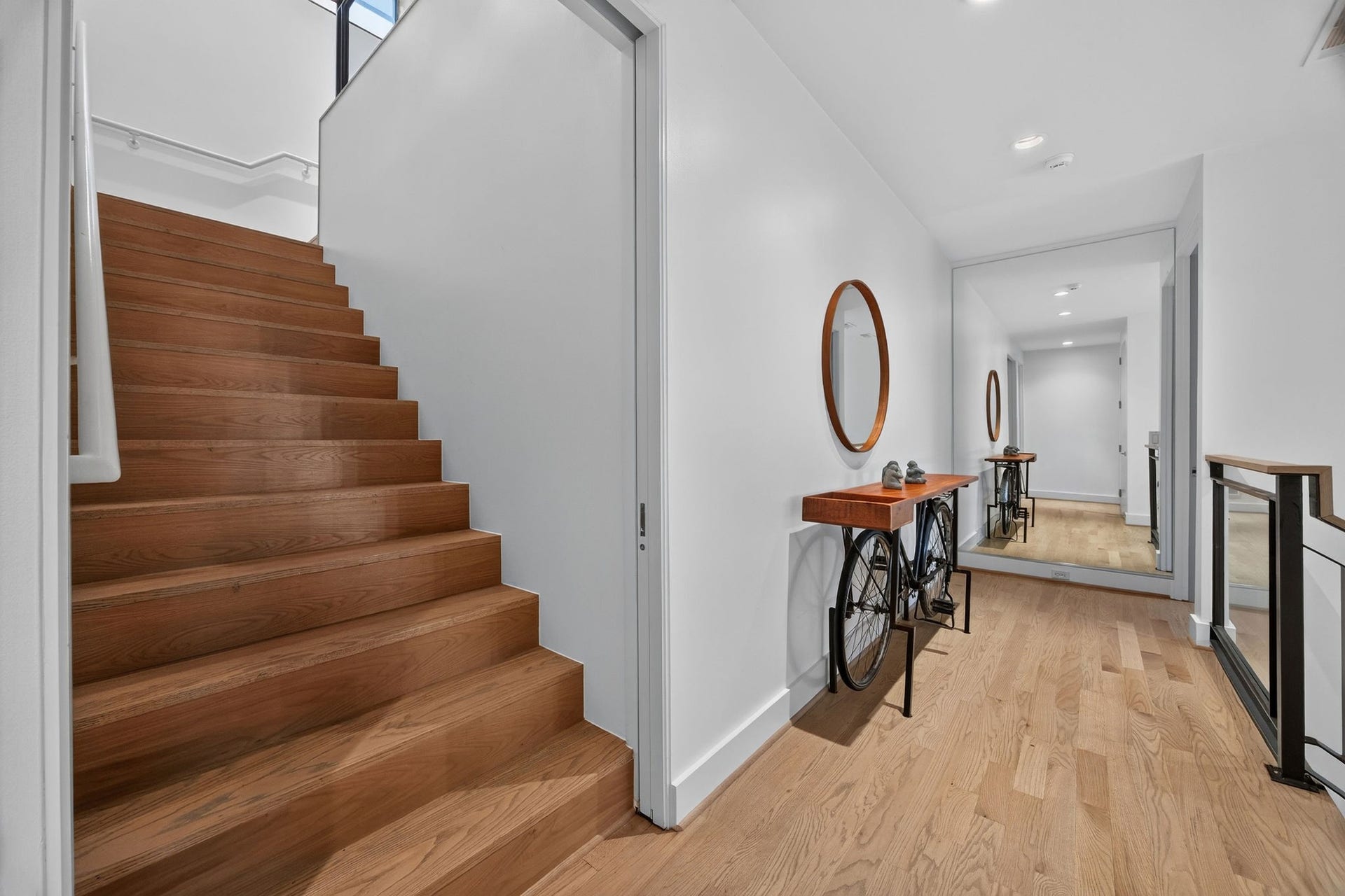 6002 Valley Forge Drive, Houston, TX 77057 Elegant modern hallway with warm wooden floors, a unique bicycle-themed console table, and a large mirror enhancing the space.