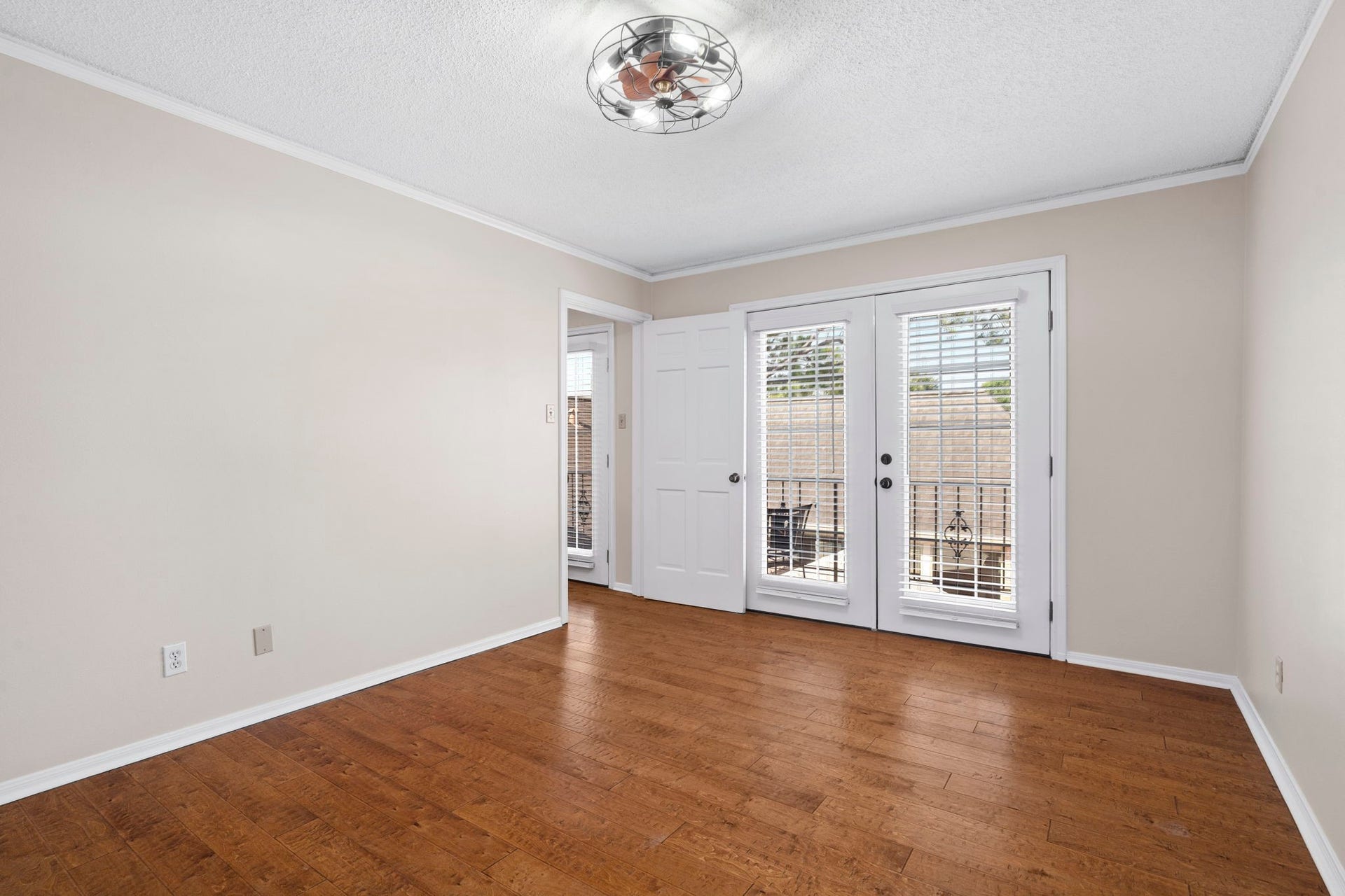 443 Fox Briar Lane, Sugar Land, TX 77478 French doors open from this inviting bedroom to a balcony overlooking the courtyard, while two closets, rich wood flooring, and a stylish cage-style ceiling fan with integrated lighting complete the space.