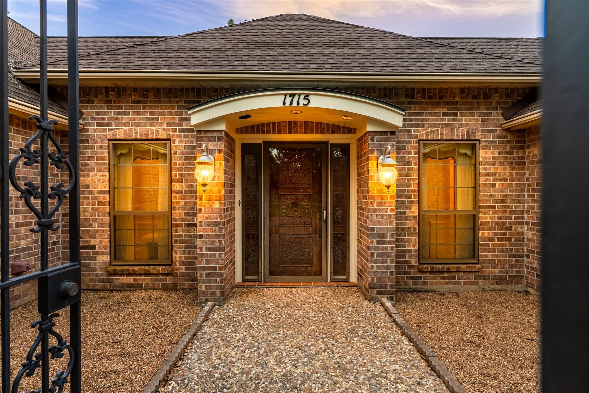 1715 Avenue D, Katy, TX 77493 Twilight accentuates the inviting courtyard and exquisitely crafted front entry, offering a glimpse of the timeless elegance that awaits inside.