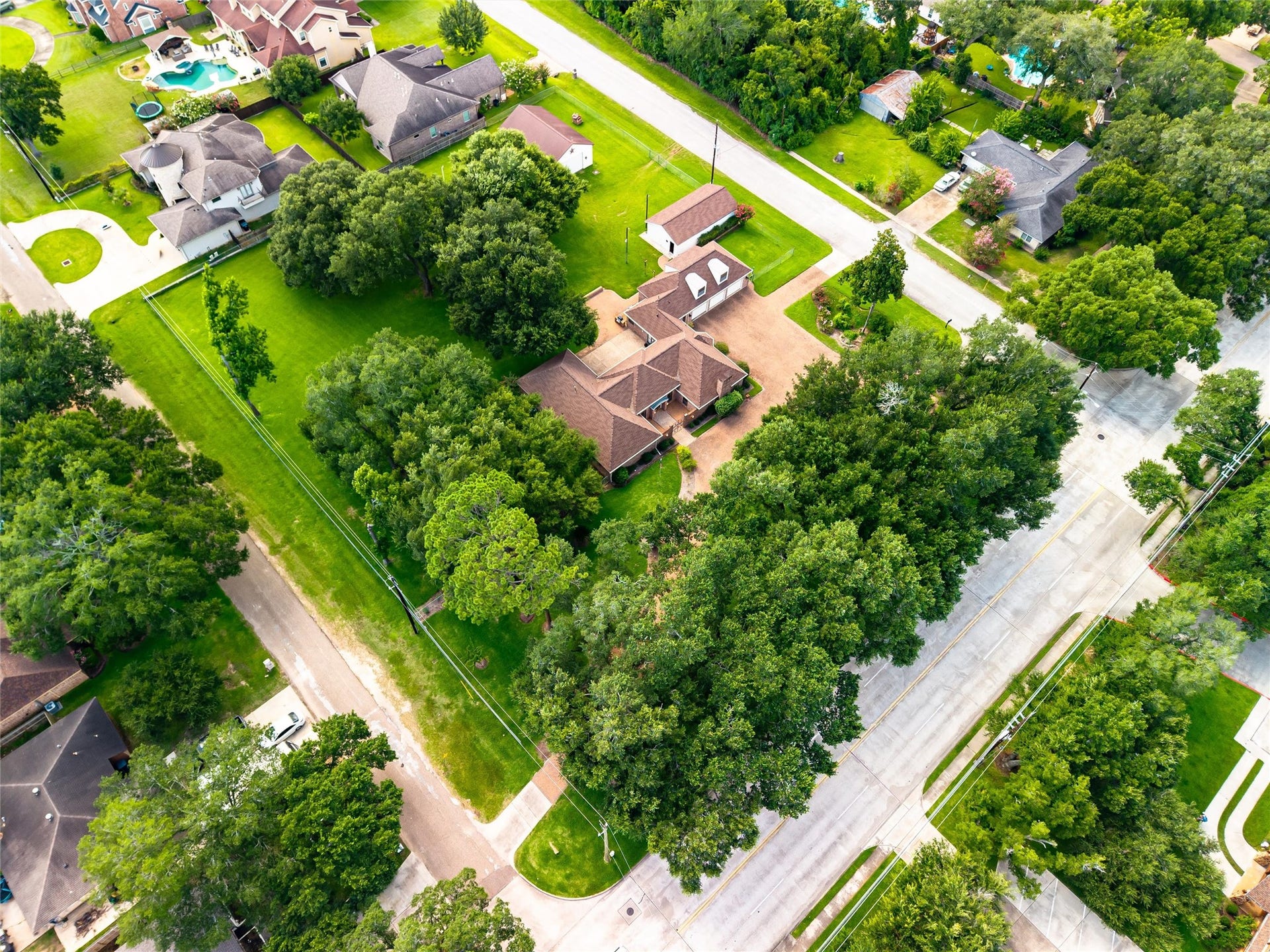 1715 Avenue D, Katy, TX 77493 This aerial perspective overlooks the thoughtful design of the 1.71-acre estate, highlighting the majestic oak canopy, sophisticated paver hardscaping, detached workshop, oversized garage and expansive grounds.