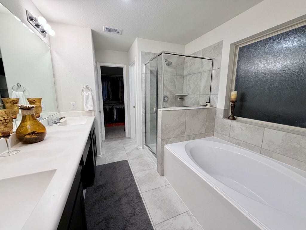 2806 Bretton Woods Drive, Conroe, TX 77301 This bathroom features a sleek design with a large vanity, double sink, and modern fixtures. It includes a spacious glass-enclosed shower and a separate soaking tub, complemented by neutral tile and a frosted window for privacy.