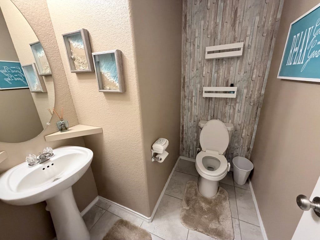 2806 Bretton Woods Drive, Conroe, TX 77301 This bathroom features a clean, modern design with neutral tones. It includes a pedestal sink, a toilet with a rustic wood accent wall that is designed for comfort.