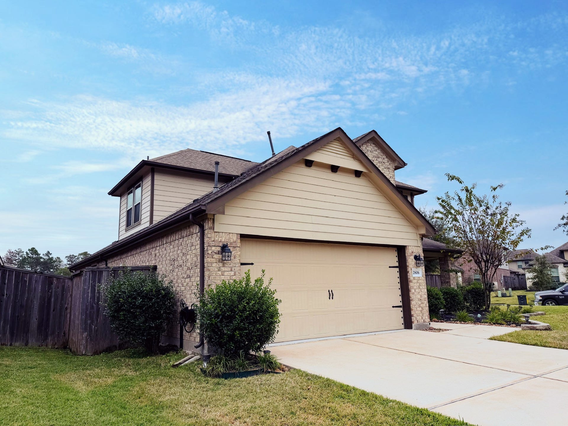2806 Bretton Woods Drive, Conroe, TX 77301 This photo features a modern two-story smart home with a brick facade and beige siding. It has a double garage, well-maintained lawn, and is situated in a suburban neighborhood. The driveway and landscaping enhance its curb appeal.