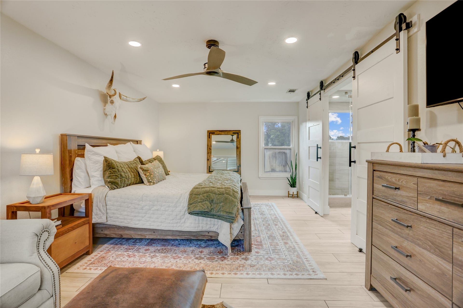3311 Carmel Valley Drive, Missouri City, TX 77459 Spacious primary suite designed for comfort and style, featuring a king sized bedroom, continued tile flooring, modern ceiling fan and sliding barn doors leading to the spa inspired en-suite bathroom.