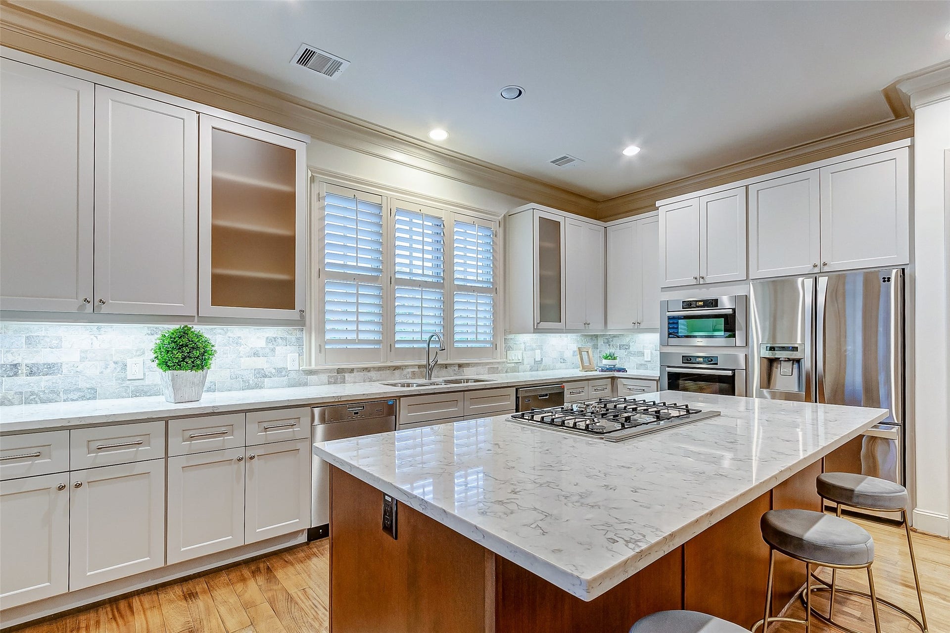 1955 Sheridan Street, Houston, TX 77030 Spacious and modern kitchen featuring sleek white cabinetry, a large marble island with a built-in cooktop, stainless steel appliances, and elegant lighting.