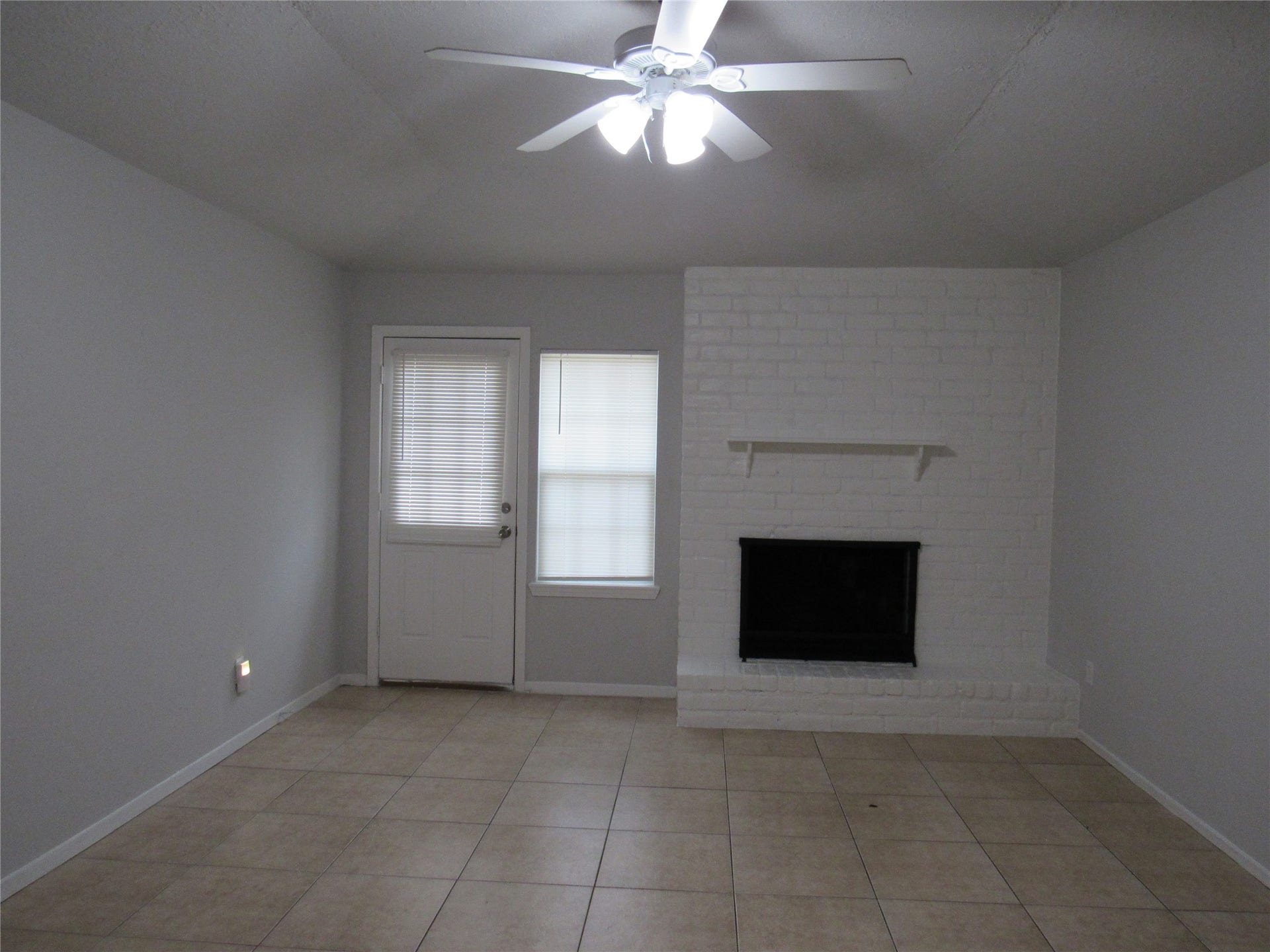 Living room w/ hi ceilings, brick WBPL, lighted fan, and door to backyard.