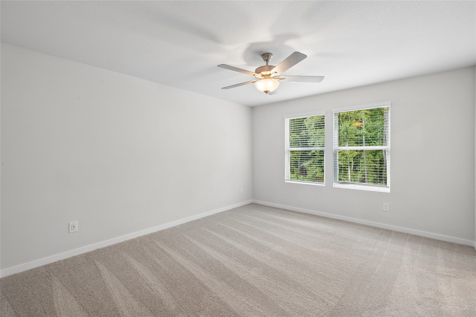 Spacious and bright room with plush carpeting, large windows offering natural light, and a ceiling fan for comfort.