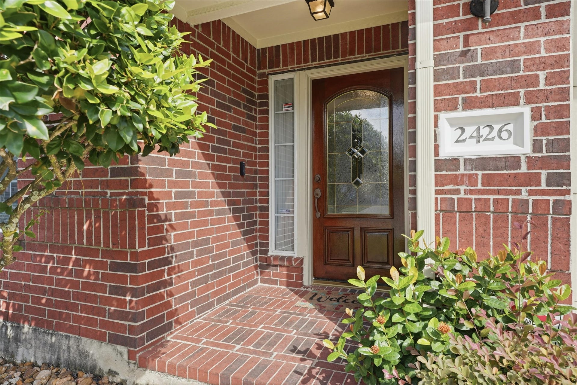 2426 Floral Ridge Drive, Spring, TX 77388 Discover the charm of this inviting front door, beautifully framed by rich brickwork and lush greenery, offering a warm welcome home.