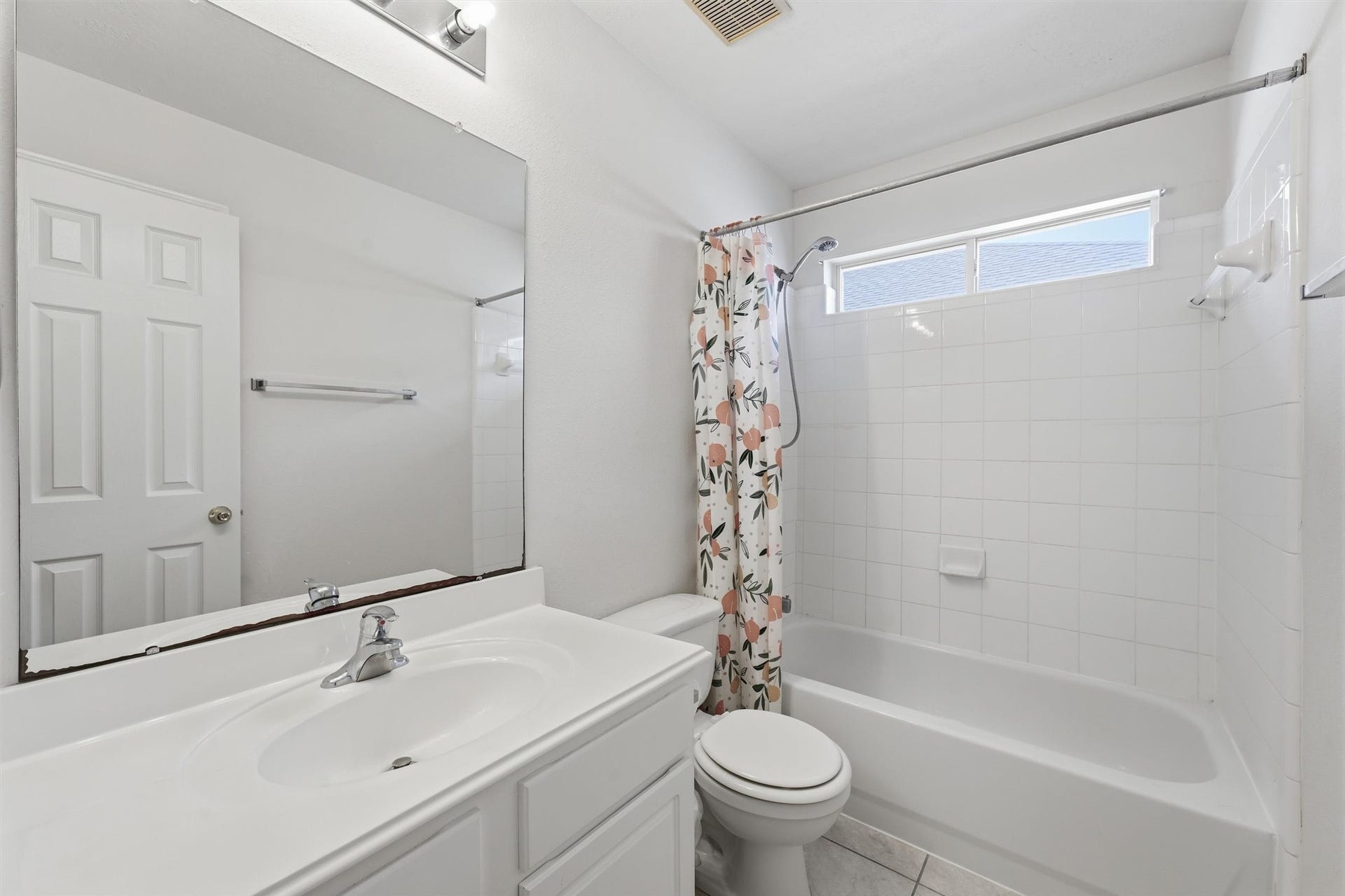 2426 Floral Ridge Drive, Spring, TX 77388 Bright and inviting bathroom featuring a clean, white vanity, spacious mirror, and a tub-shower combination with a floral curtain.