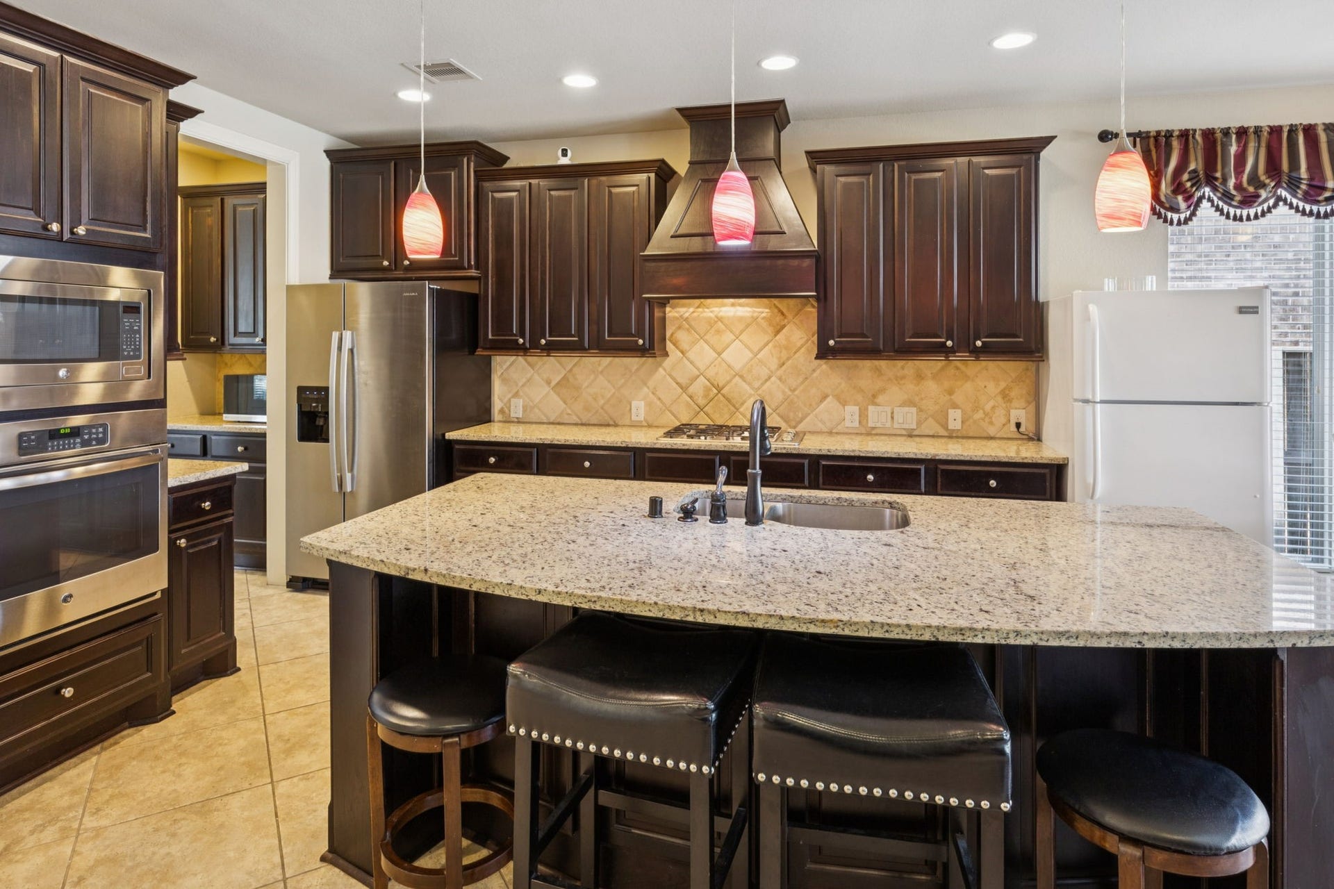 The elegant tile backsplash and decorative vent hood create a refined ambiance for both daily meals and high-end entertaining.