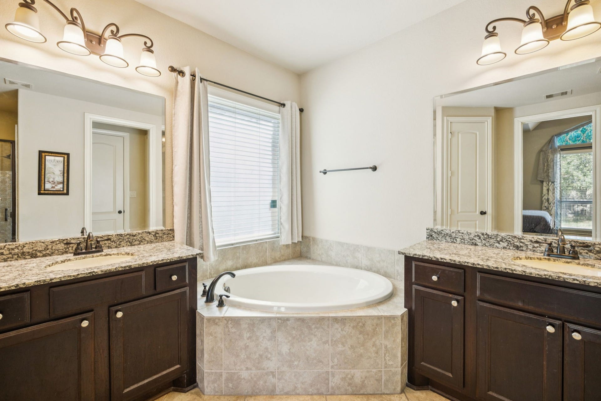 Relax in this spa-inspired primary bathroom featuring dual granite vanities and a large garden soaking tub. The space includes a glass-enclosed shower and tile flooring.