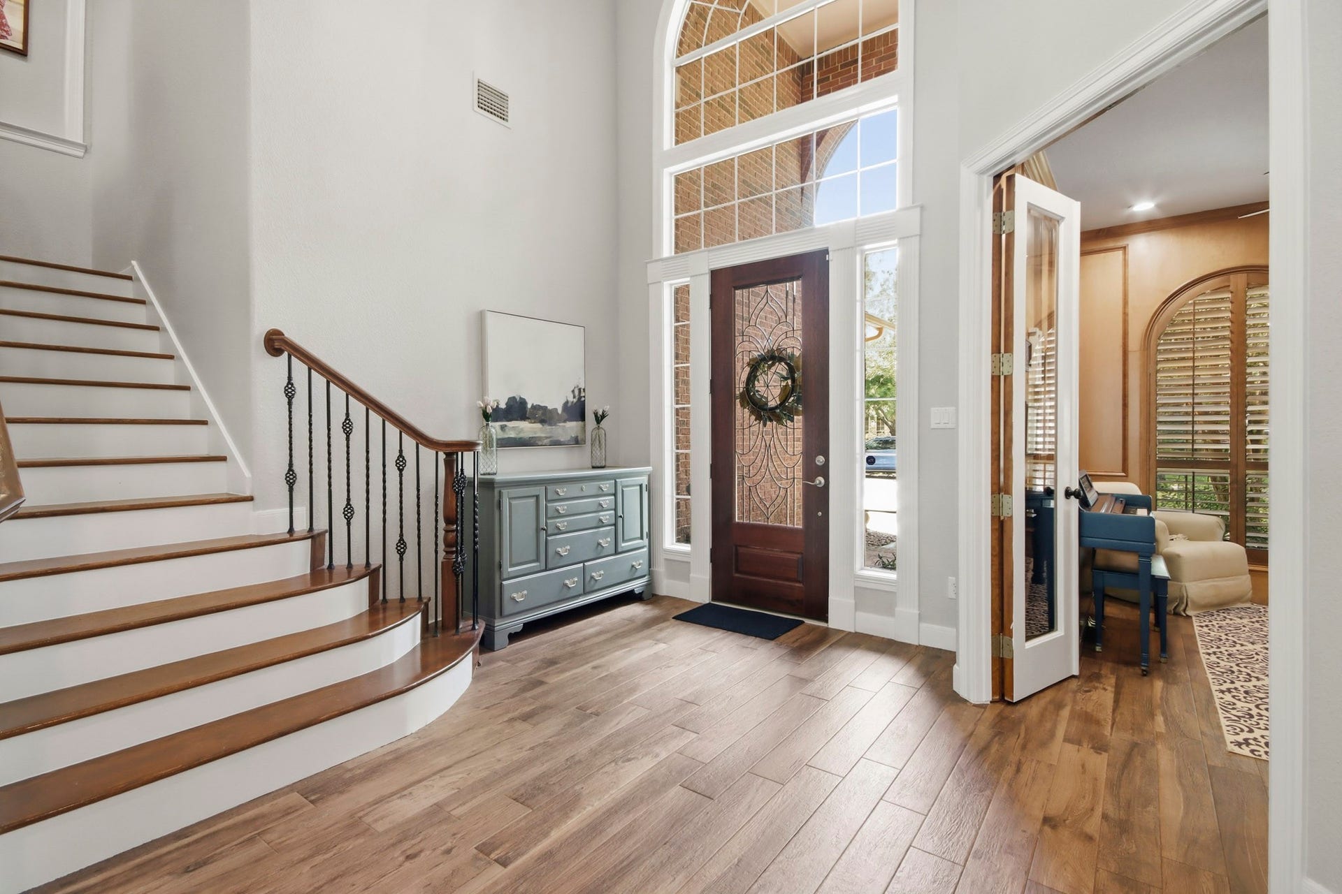 Elegant entryway with rich wood-like tile floors, a graceful wooden staircase, and an inviting open floor plan leading to spacious living areas.