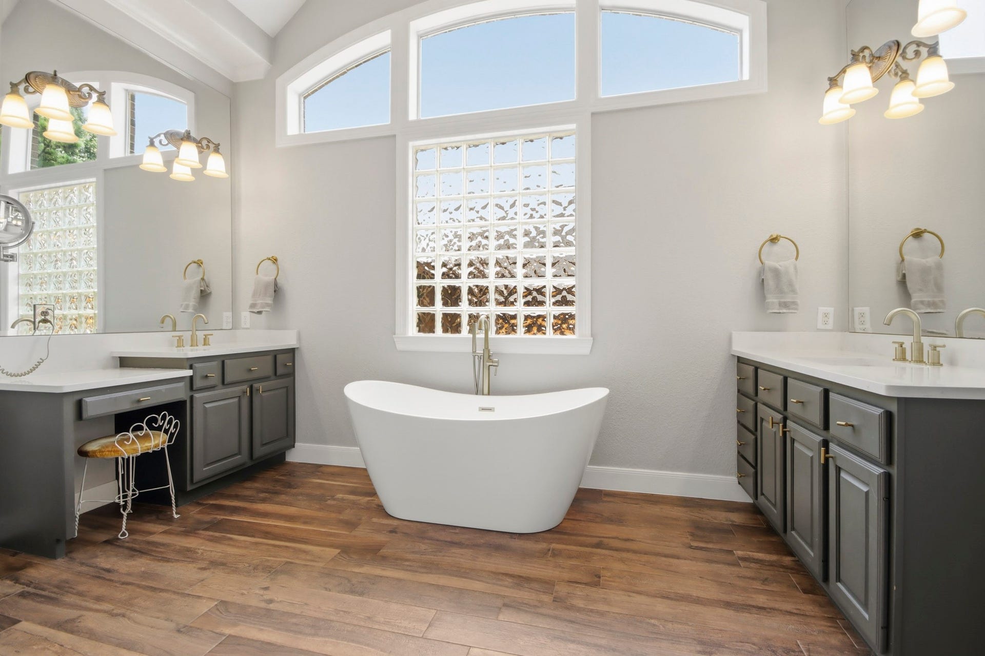 Luxurious bathroom featuring a beautiful freestanding tub, dual vanities with elegant fixtures, and abundant natural light through arched windows.