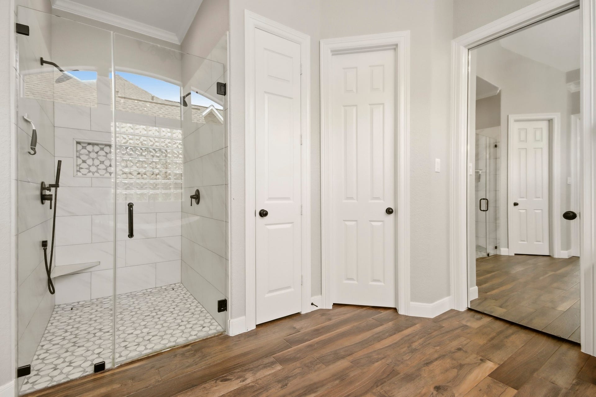 The Primary bathroom includes a spacious glass-enclosed shower with modern fixtures, stylish tile work, and warm wood-like tile flooring.