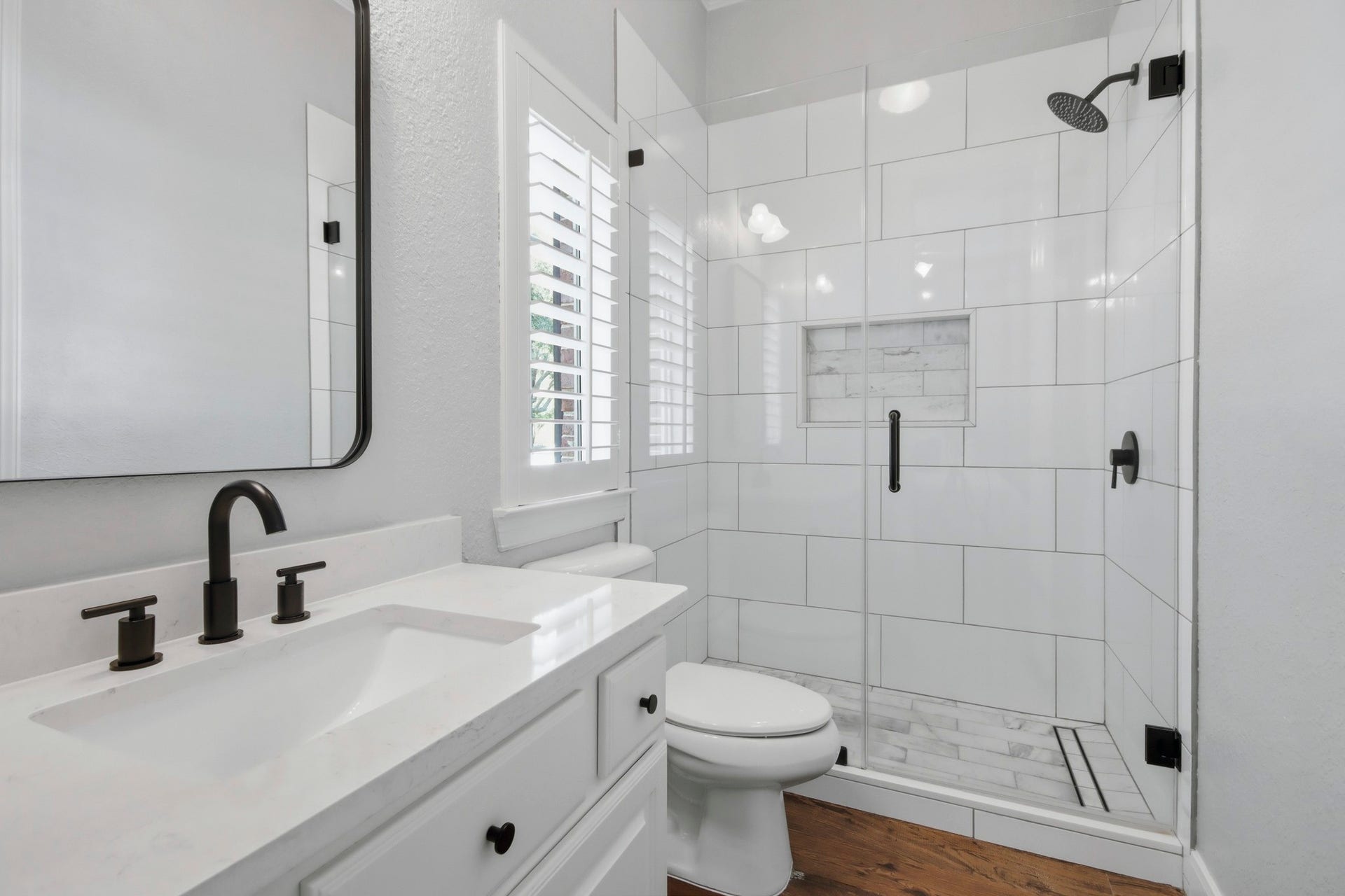 Updated modern downstairs en-suite bathroom featuring a spacious glass-enclosed shower, white tile, and stylish black fixtures for a contemporary touch.