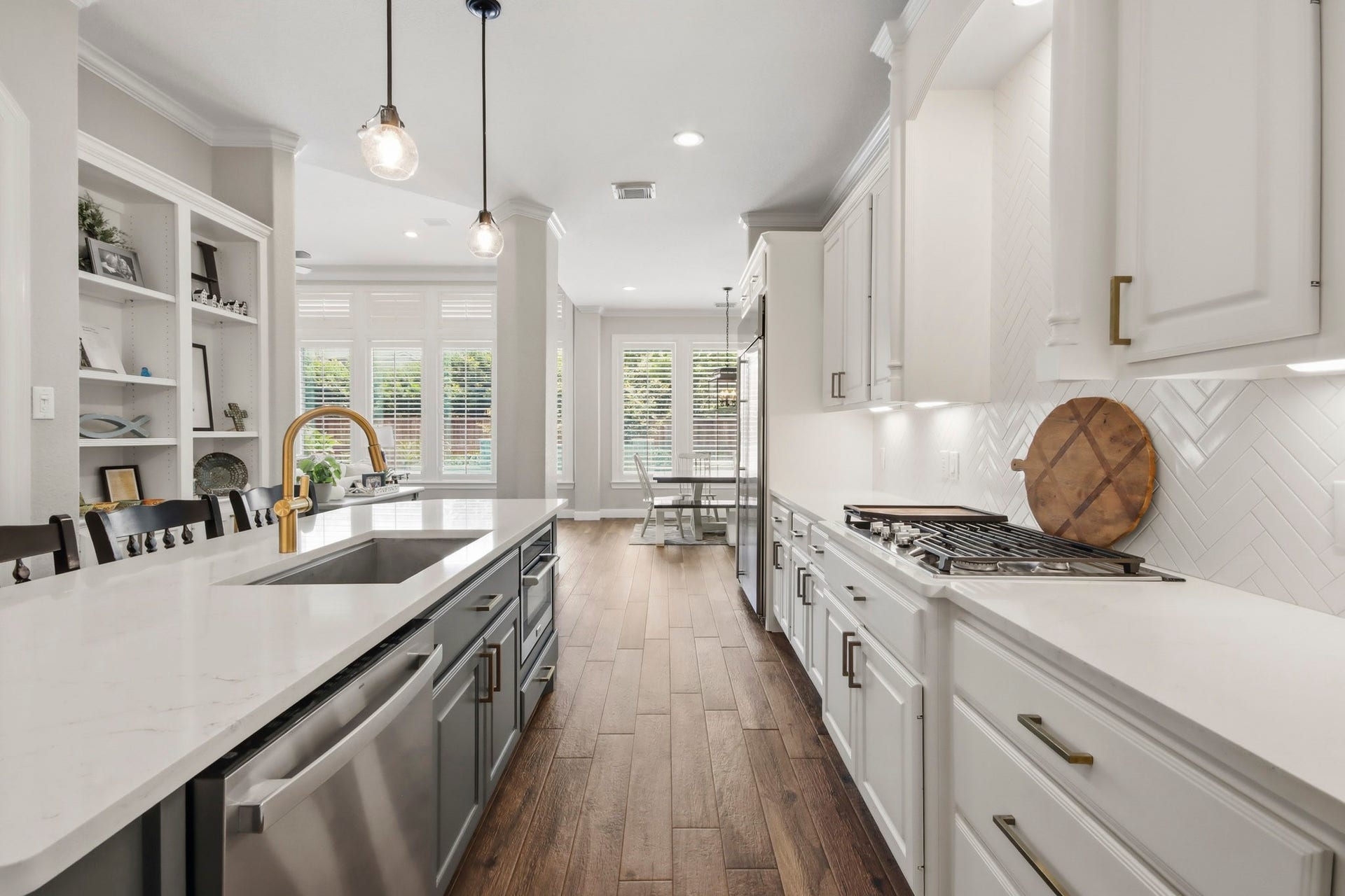 The open layout features a spacious island and a stylish gold faucet, all set against warm wood-like tile flooring and illuminated by sleek pendant lighting.