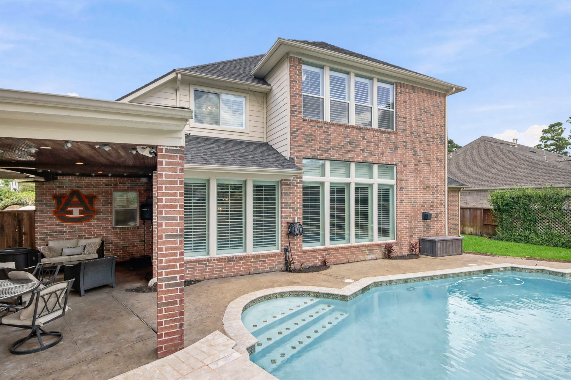 Charming two-story brick home with a refreshing pool and cozy covered patio, perfect for outdoor relaxation and entertaining.
