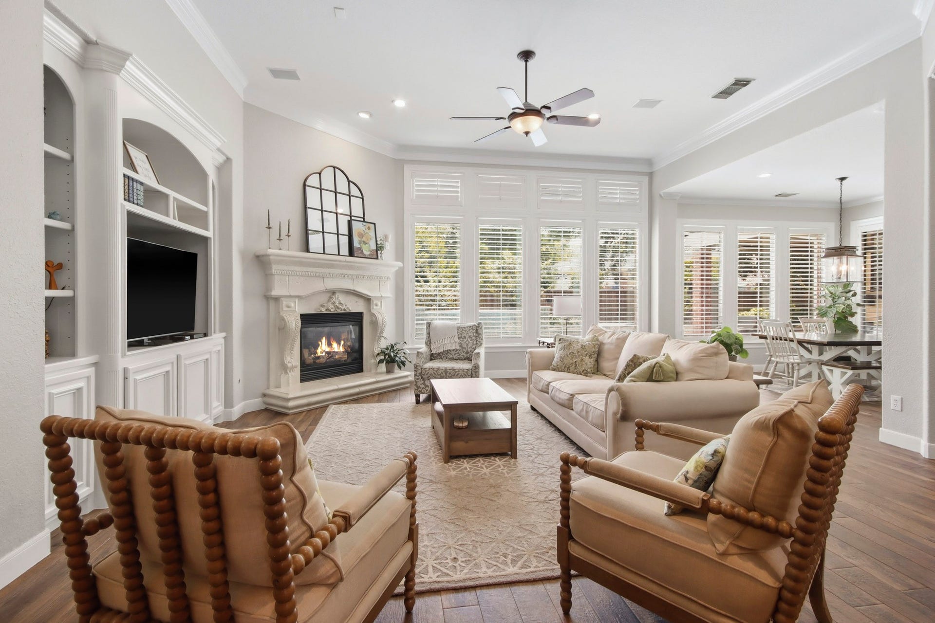 Living room with a cozy fireplace, built-in shelving, and abundant natural light from expansive windows with plantation shutters.