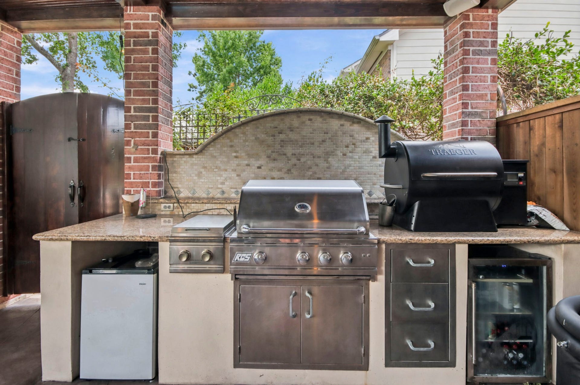 Outdoor kitchen with stainless steel grill, and mini fridge, set against a stylish stone backsplash and brick accents, perfect for entertaining.