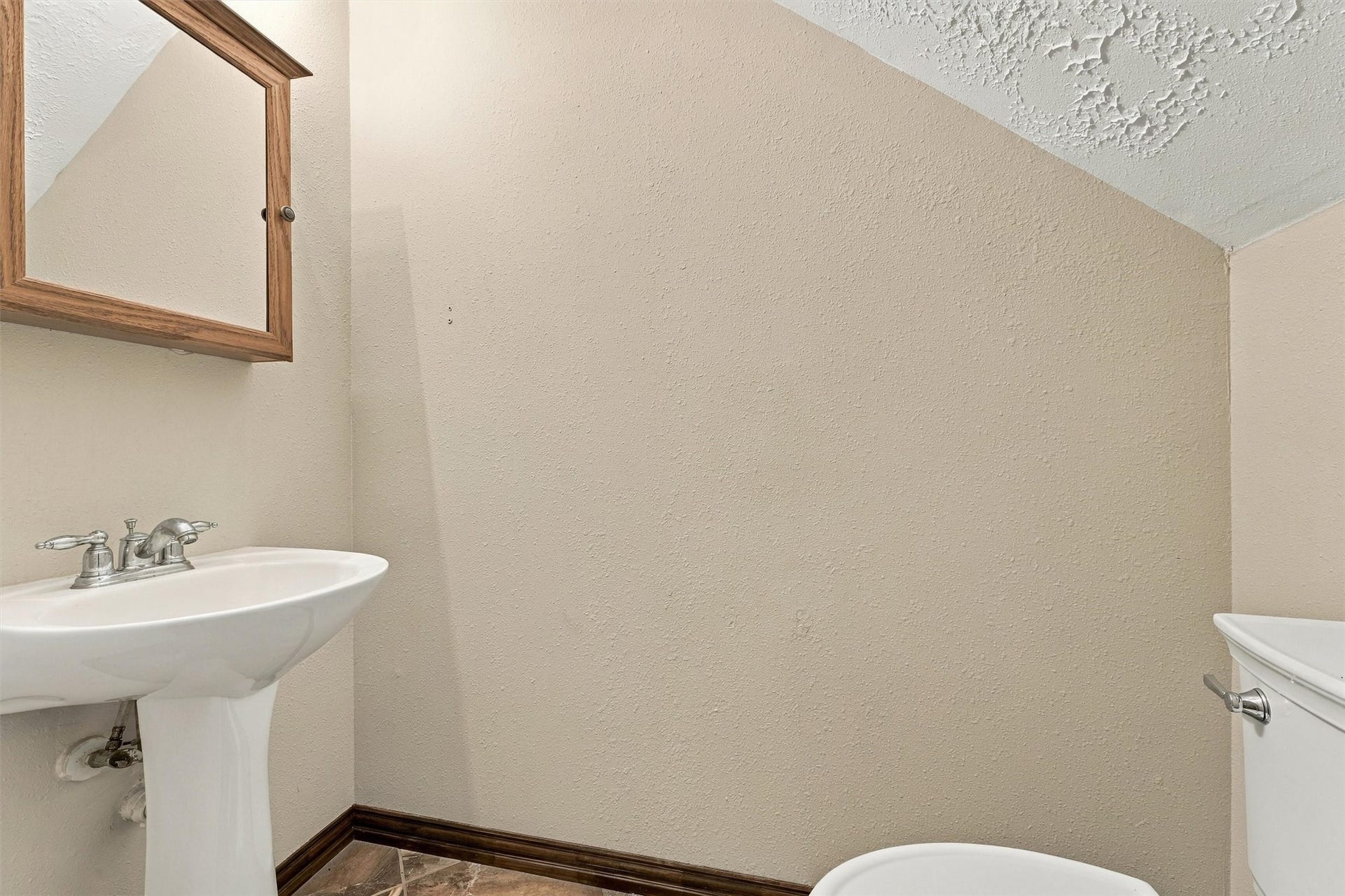 Cozy powder room featuring a classic pedestal sink and a wooden-framed mirror, perfect for guest use.