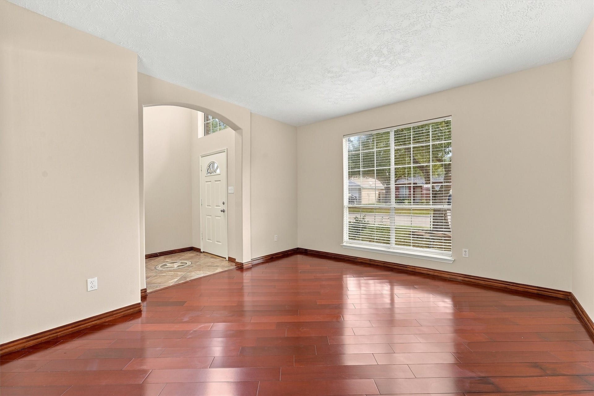 Bright and inviting living space featuring rich hardwood floors, a large front window for natural light, and elegant archway leading to the entryway.