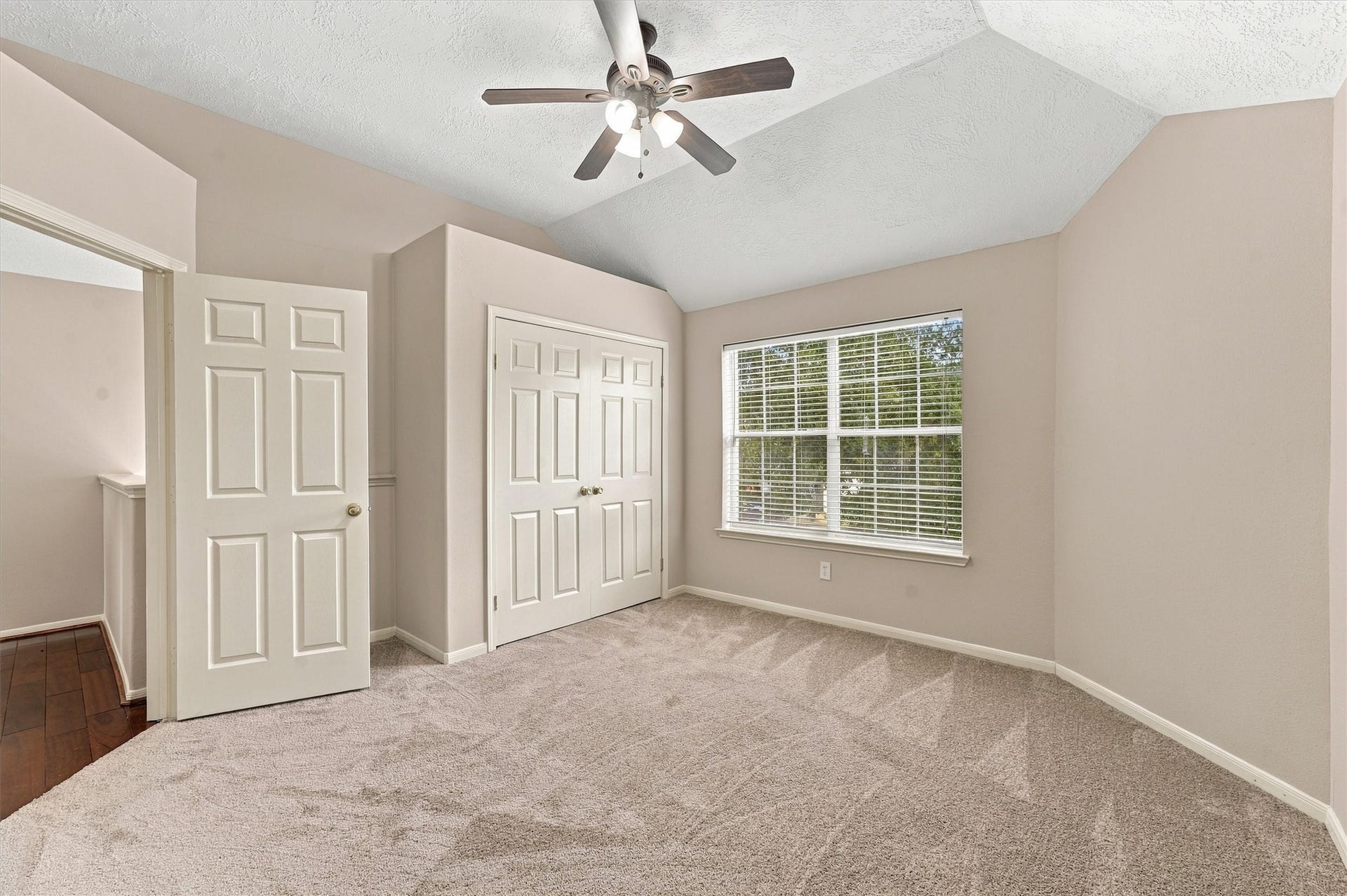 Bright and inviting bedroom featuring plush carpeting, a ceiling fan, and ample natural light from a large window, complemented by double-door closet space.