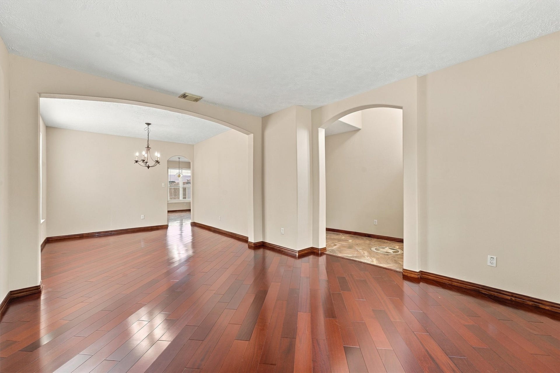 Elegant open-concept living area featuring rich hardwood floors, archways, and a stylish chandelier, perfect for entertaining and family gatherings.