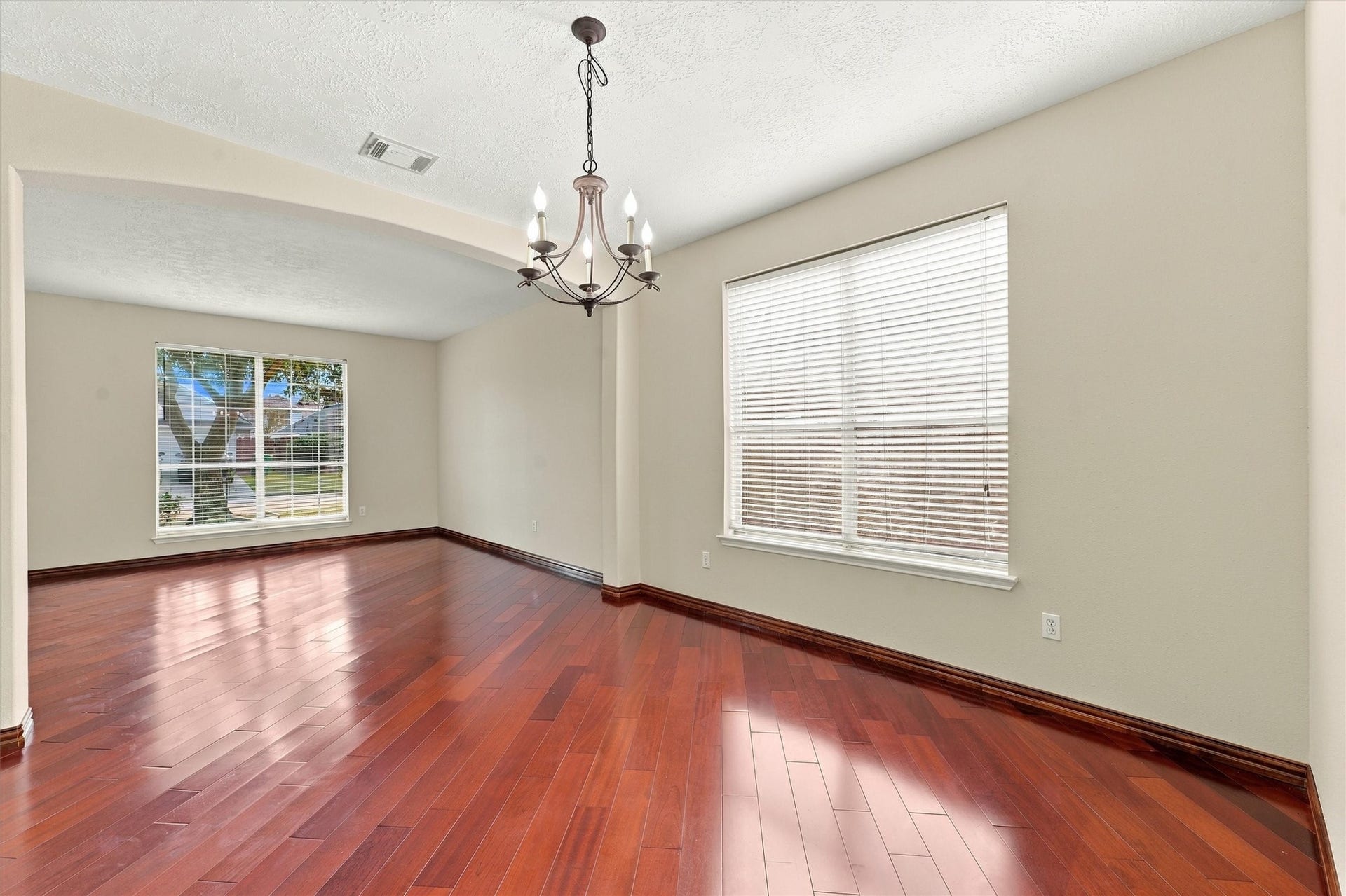 Elegant open living space featuring rich hardwood floors, abundant natural light from large windows, and a stylish chandelier for a touch of sophistication.