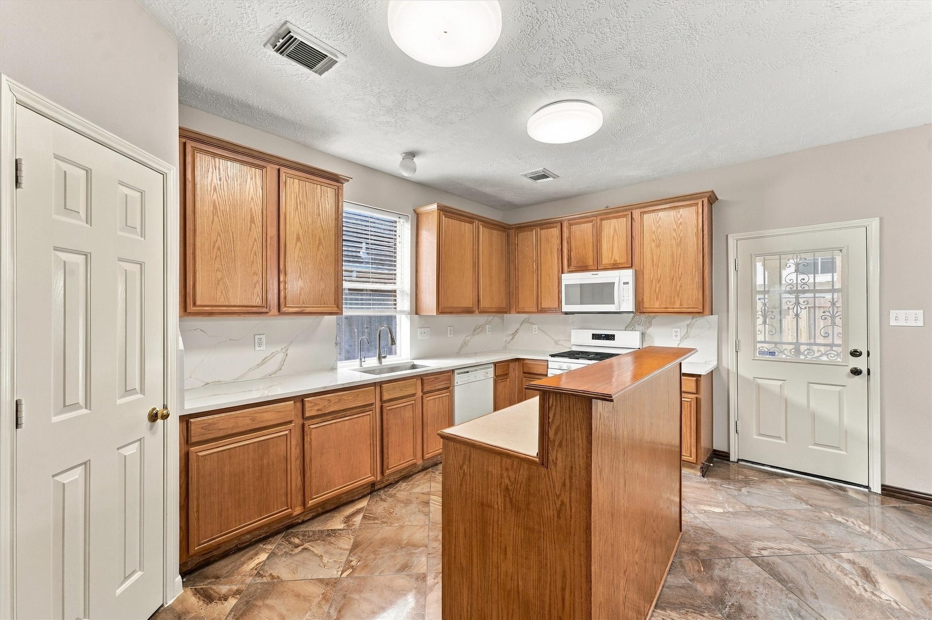 Spacious kitchen featuring warm wooden cabinetry, sleek marble countertops, and modern appliances, offering ample storage and workspace for culinary enthusiasts.