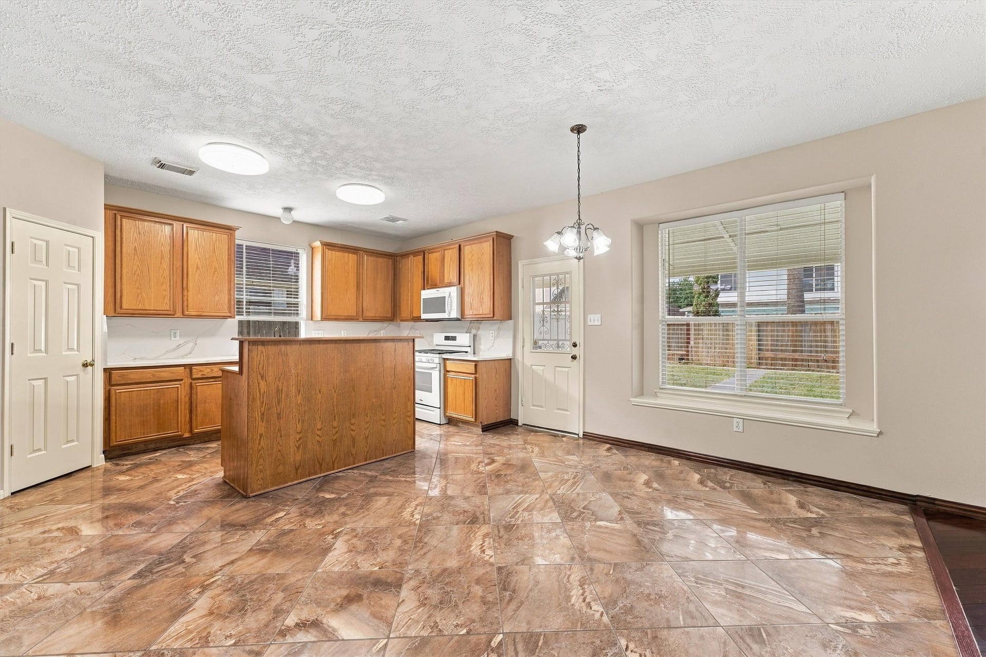 Bright and spacious kitchen with warm wood cabinetry, modern appliances, and elegant tile flooring, seamlessly flowing into a cozy dining area with natural light from a large window.