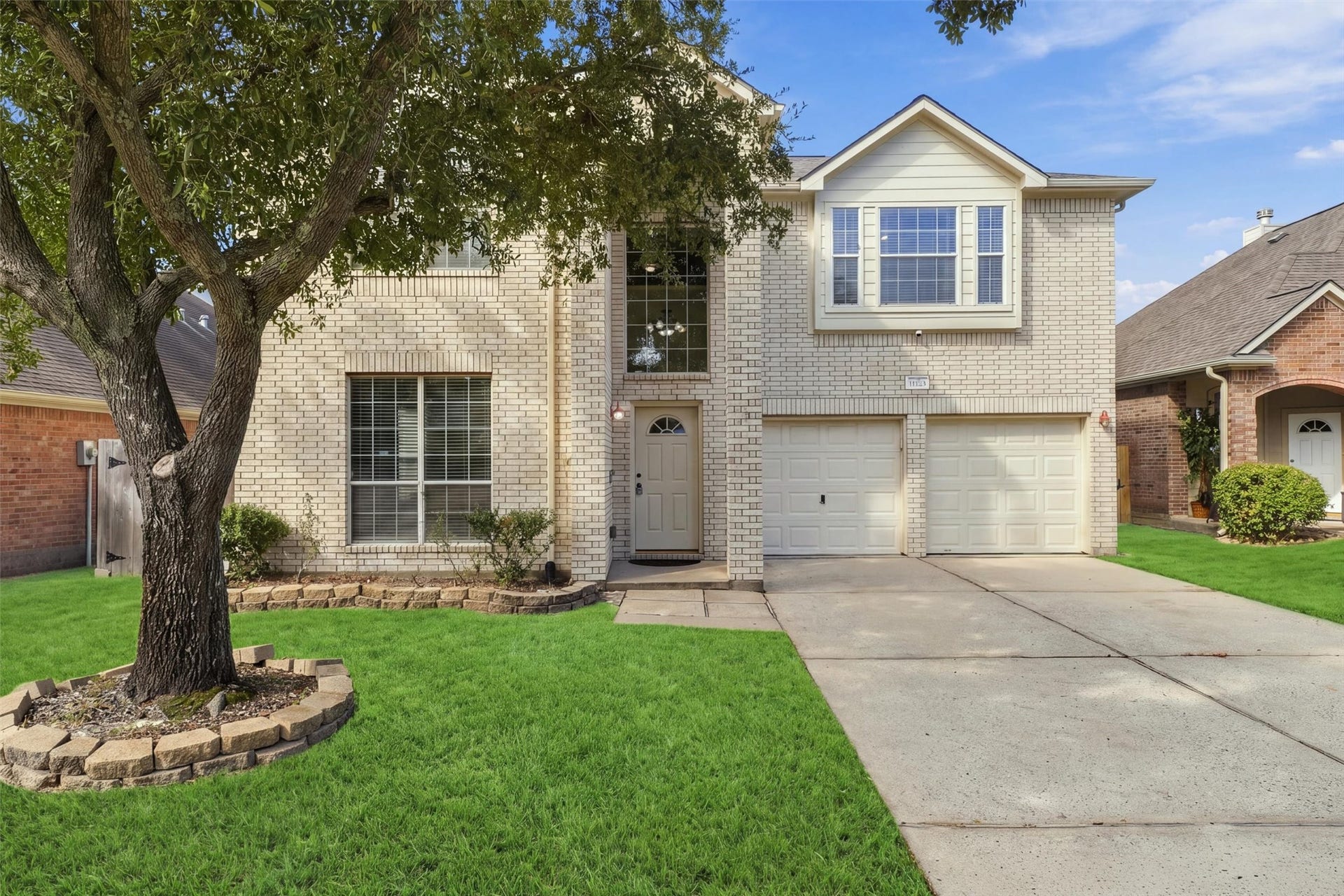 Charming two-story brick home with a welcoming front yard and a spacious driveway leading to a double garage.