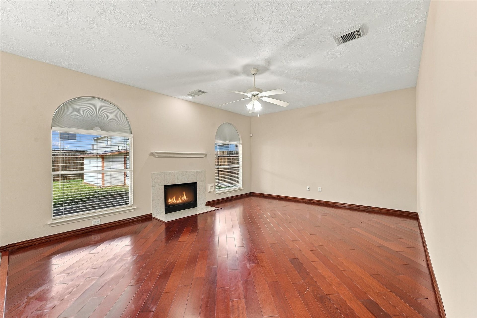 Spacious living room with rich hardwood floors, a cozy fireplace, and abundant natural light from large arched windows, creating a warm and inviting atmosphere.