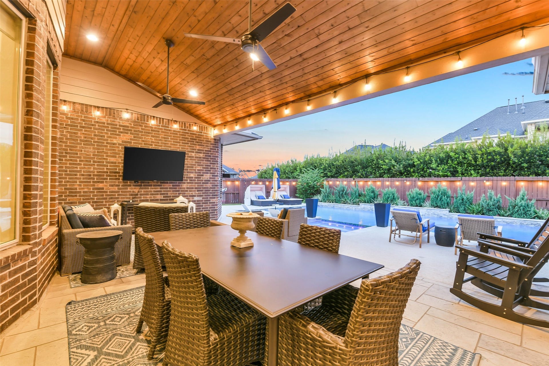 5410 Briarcliff Lane, Fulshear, TX 77441 Step outside to outdoor living at its finest with this stunning covered patio featuring a beautiful tongue-and-groove wood ceiling, dual ceiling fans, and recessed lighting. Overlooking the sparkling pool and surrounded by lush landscaping, this thoughtfully designed space is perfect for dining, entertaining, and relaxing year-round.
