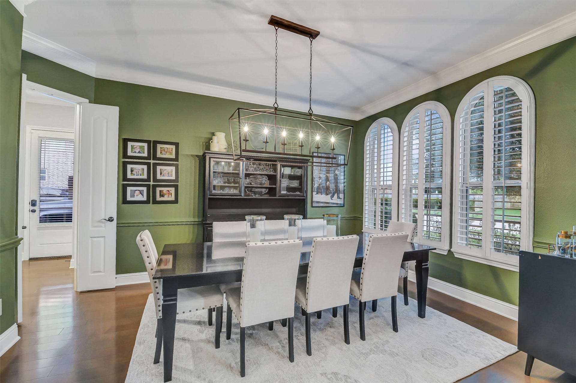 5410 Briarcliff Lane, Fulshear, TX 77441 An elegant formal dining room highlighted by a stunning wall of arched windows with plantation shutters, hardwood flooring, crown molding, and a statement chandeliercreating the perfect setting for memorable gatherings and special occasions