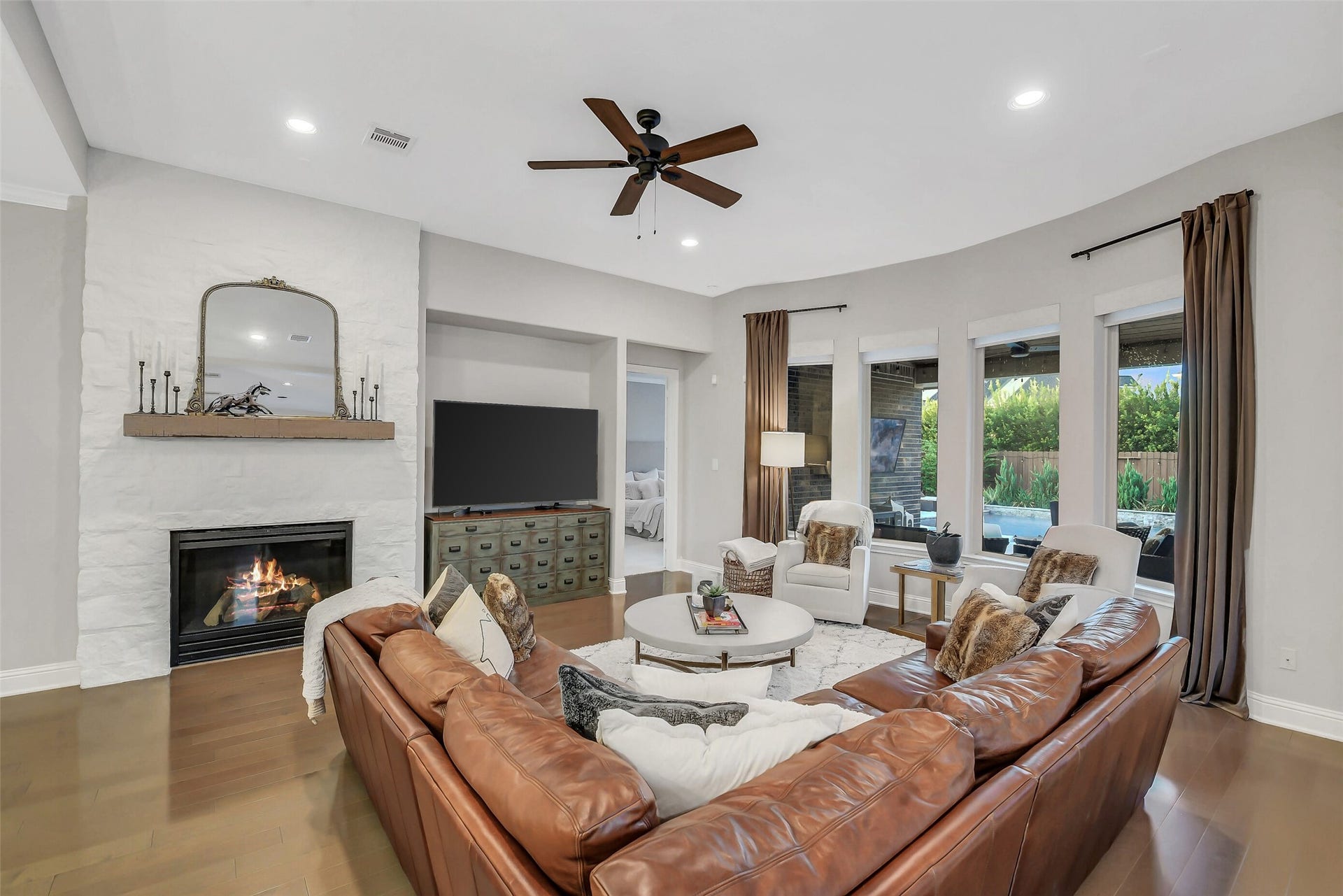 5410 Briarcliff Lane, Fulshear, TX 77441 The welcoming family room features a dramatic stone fireplace and expansive windows overlooking the serene backyard retreat.