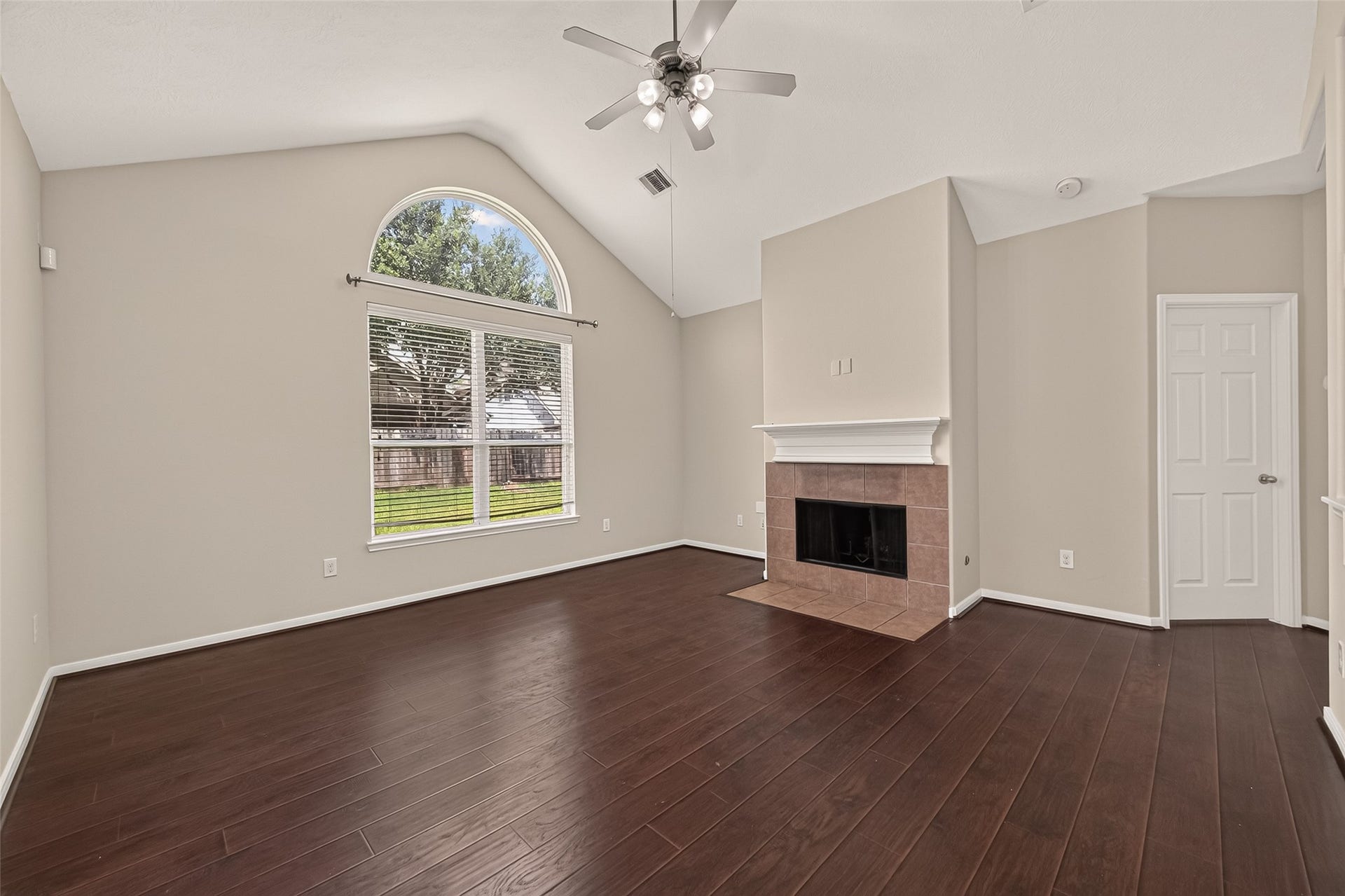 3635 Cottage Manor Lane, Katy, TX 77494 Open living room with a vaulted ceiling, ceiling fan, arched window, tiled fireplace, and wood-look flooring throughout.