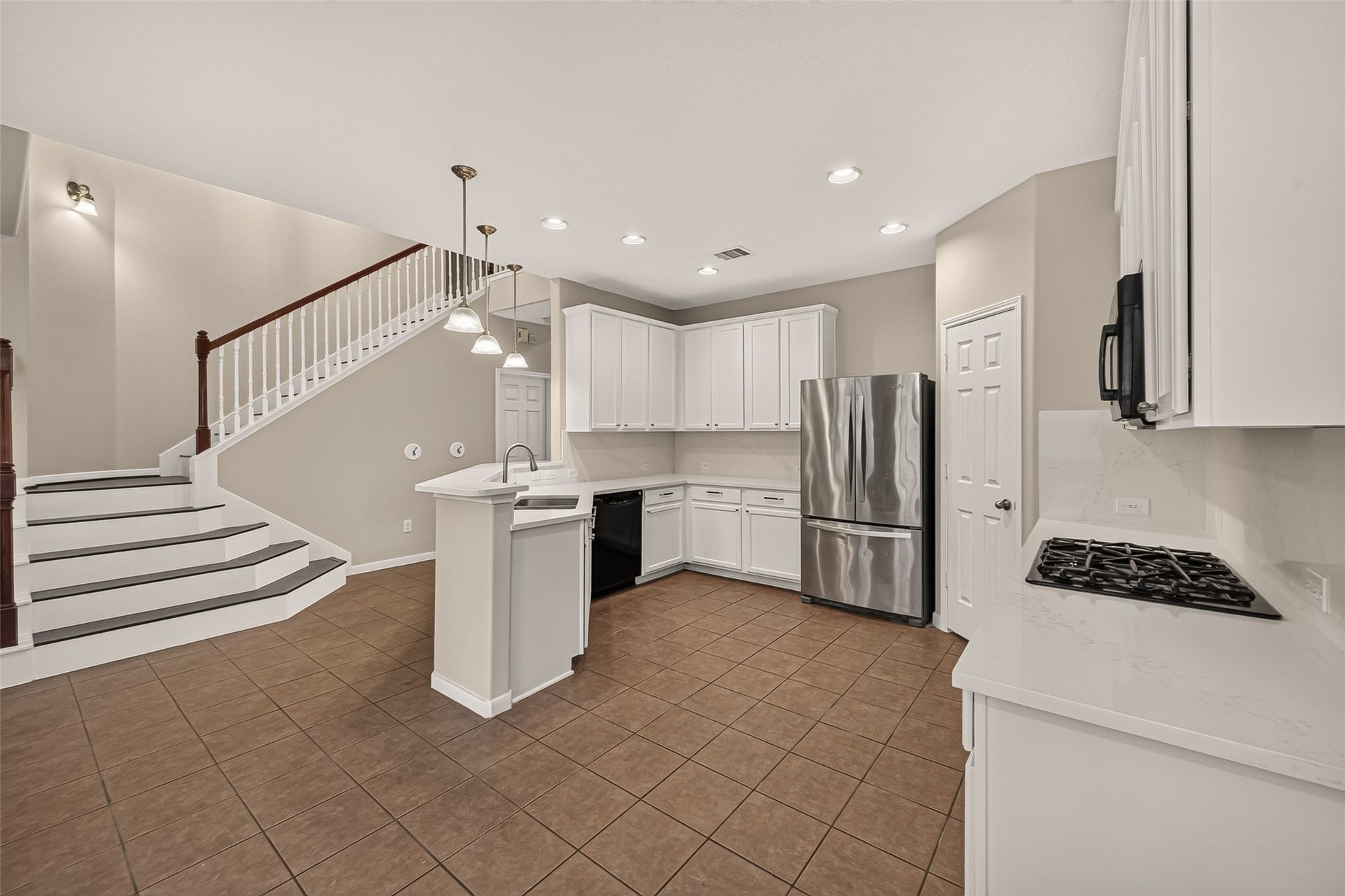 3635 Cottage Manor Lane, Katy, TX 77494 Bright kitchen featuring white cabinetry, lightly veined countertops, a gas cooktop, and a stainless steel French-door refrigerator. Pendant lighting accents the raised breakfast bar, with the open staircase adding architectural interest.