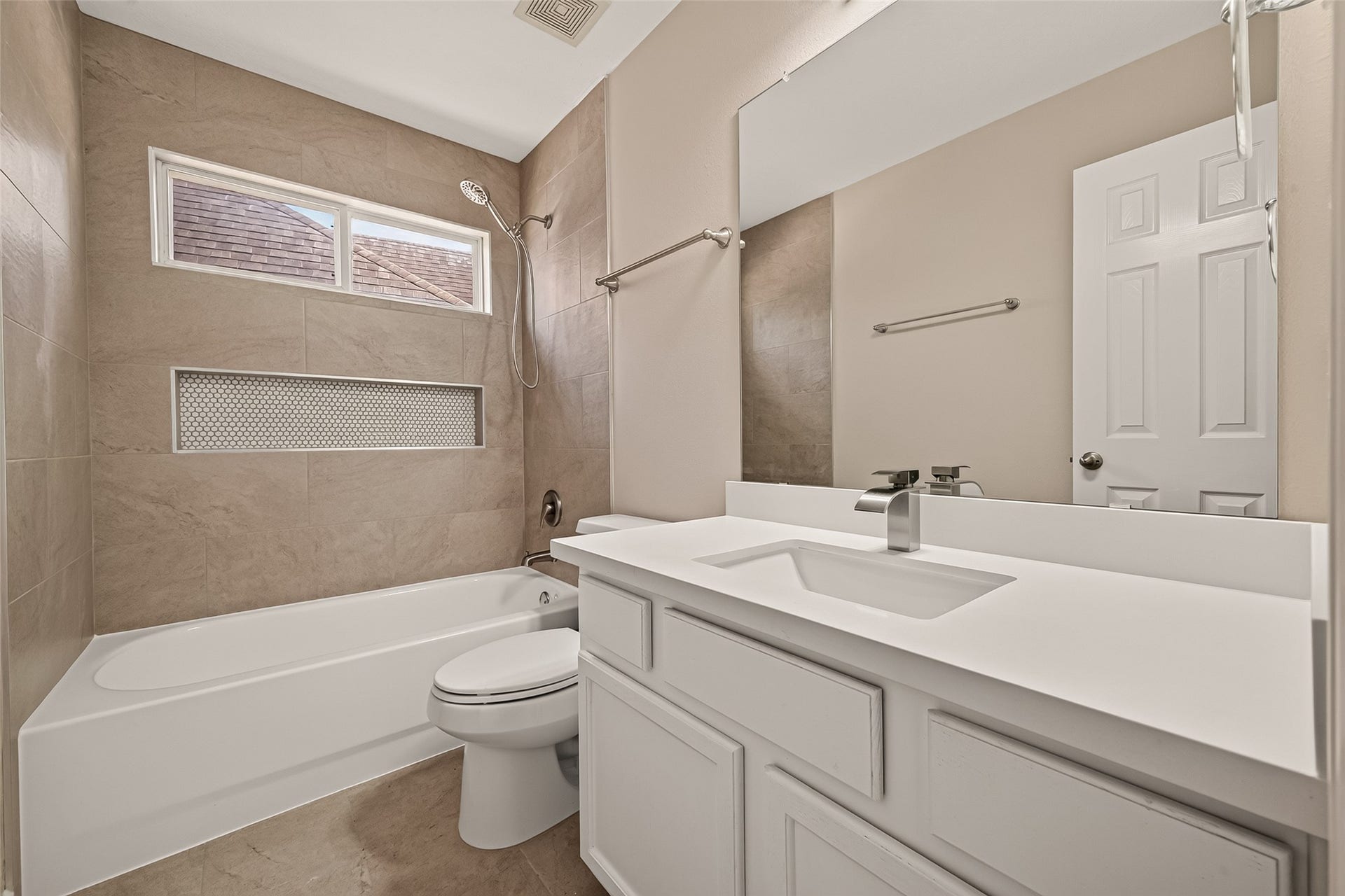 3635 Cottage Manor Lane, Katy, TX 77494 Updated bath with a tub/shower combo, large-format tile surround, penny-tile niche, handheld showerhead, and a white vanity with an undermount sink and waterfall faucet.