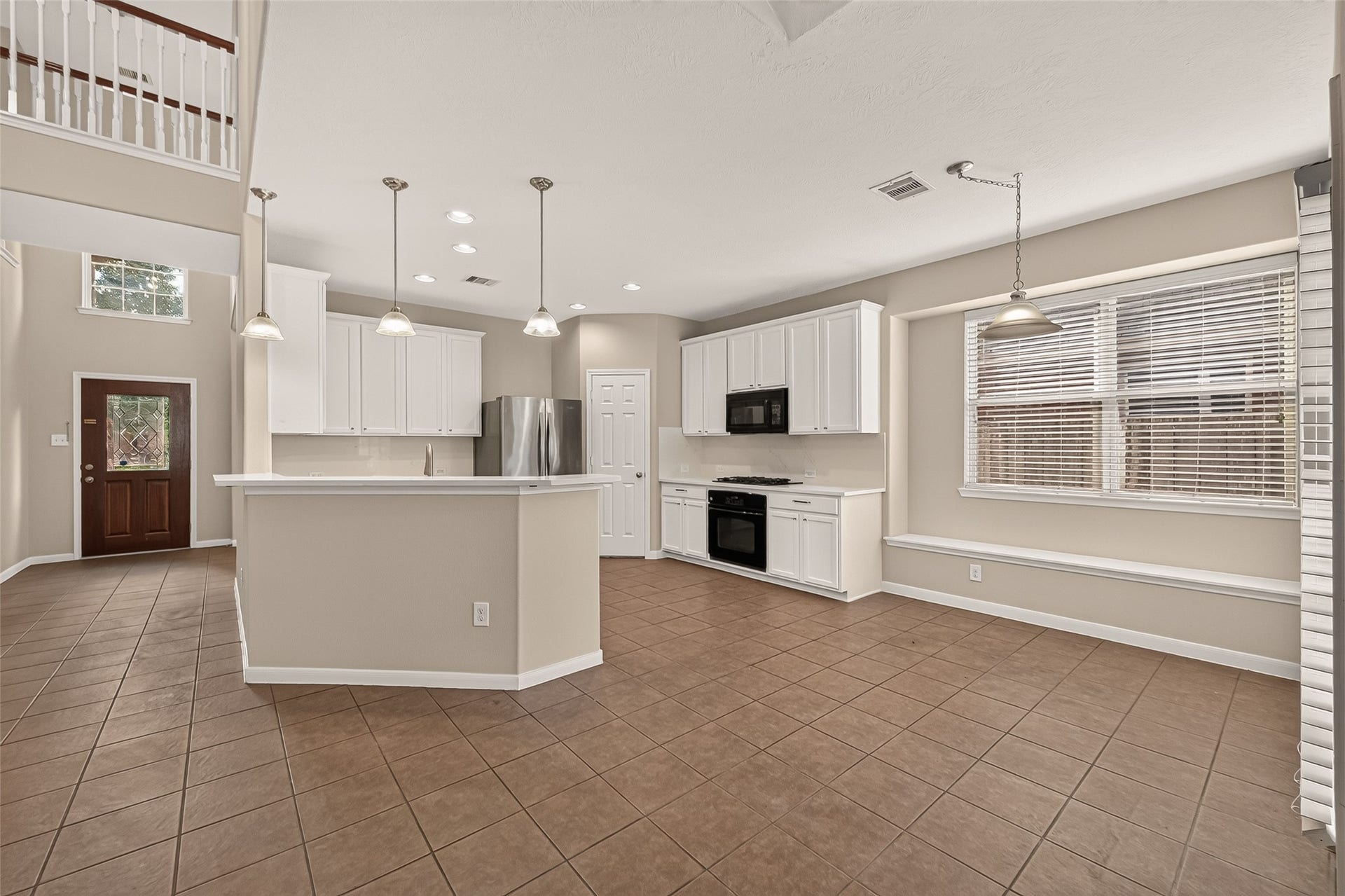 3635 Cottage Manor Lane, Katy, TX 77494 Open kitchen and breakfast area featuring a raised breakfast bar, pendant lighting, and white cabinetry. Large windows and built-in window seating brighten the dining space, while warm tile flooring connects the adjoining areas.
